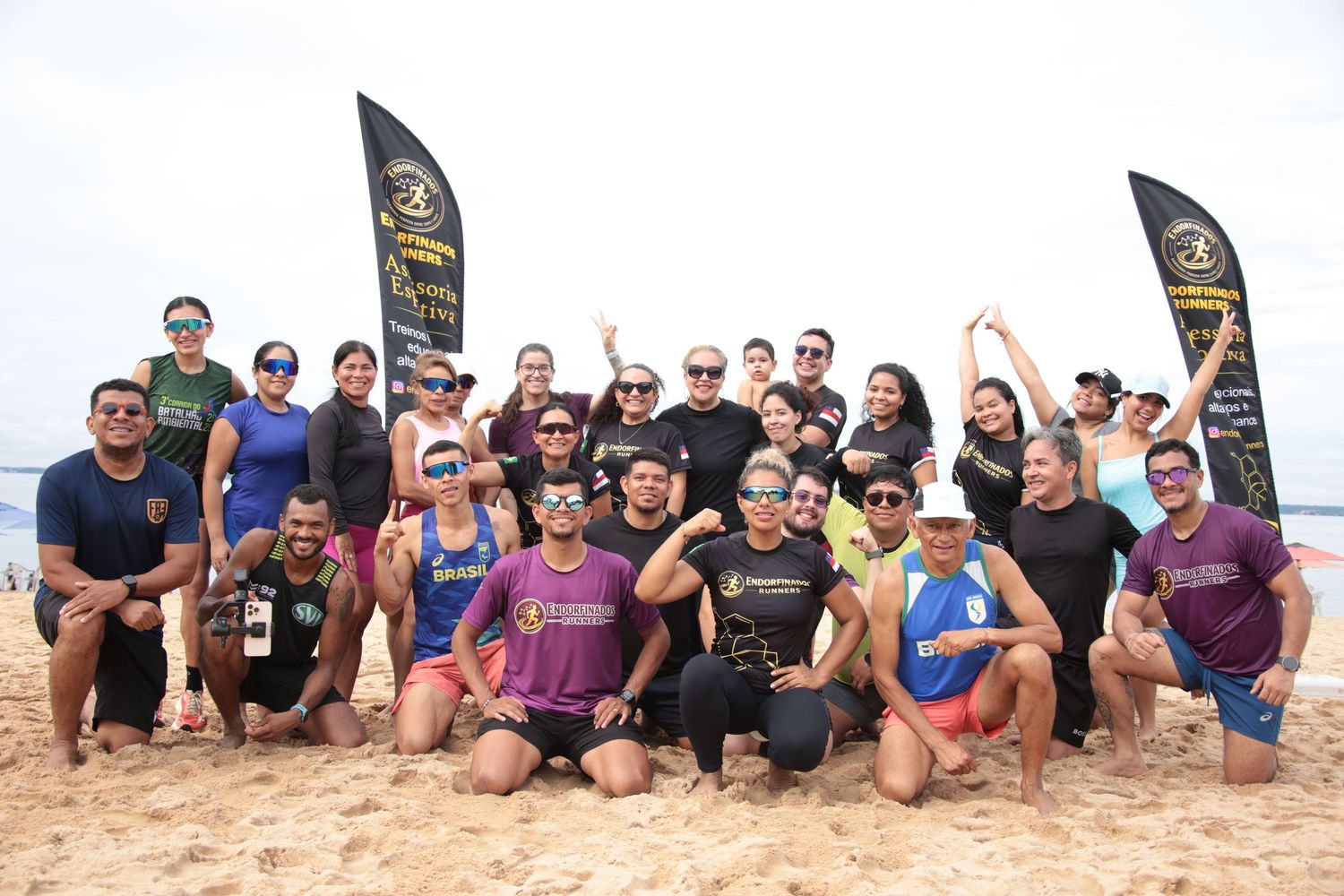 Diverse fitness group posing on sandy beach with black promotional banners during outdoor sports event.