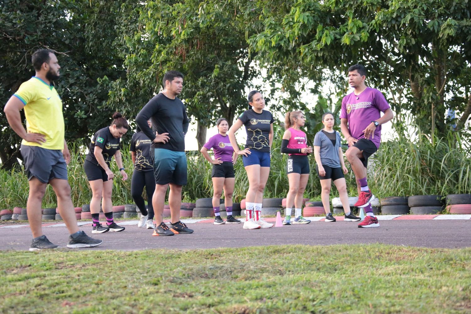 Running coach in yellow shirt leads stretching warmup with group of athletes in park.
