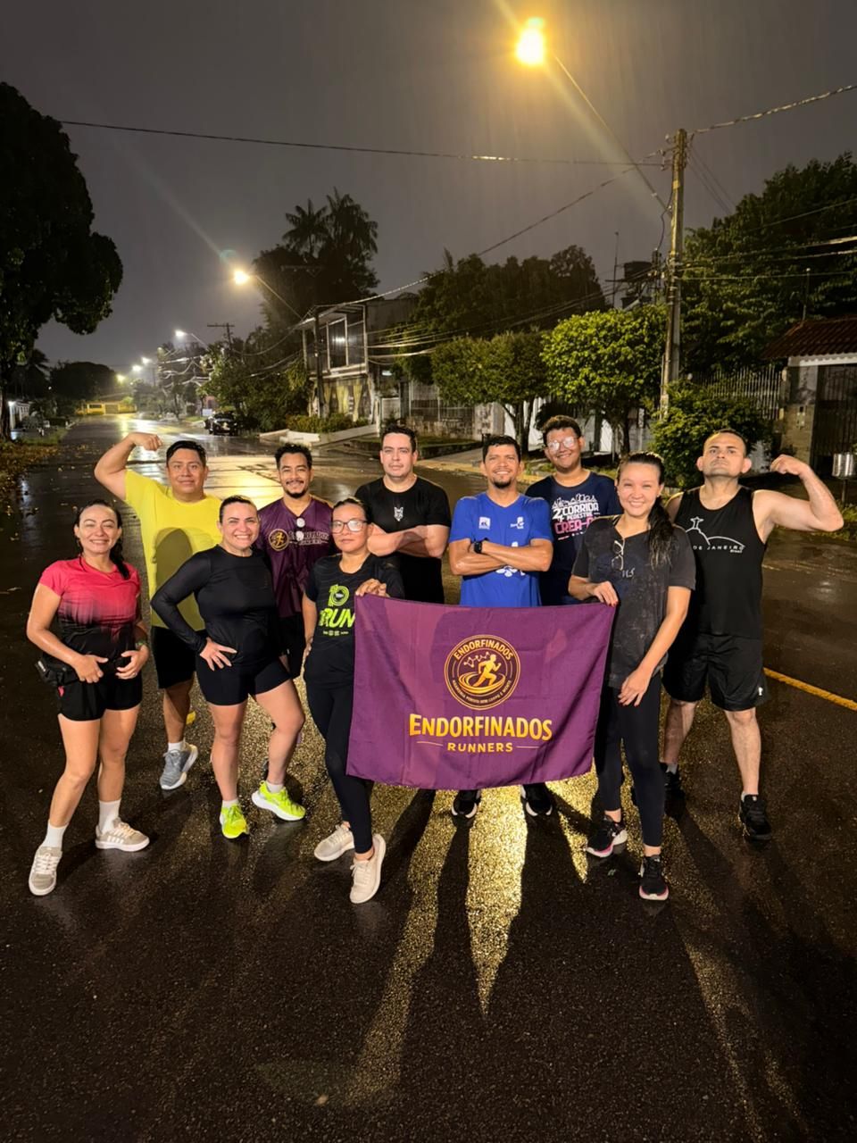 Group of runners posing at night holding a purple Endorfinados Runners banner on a wet street.