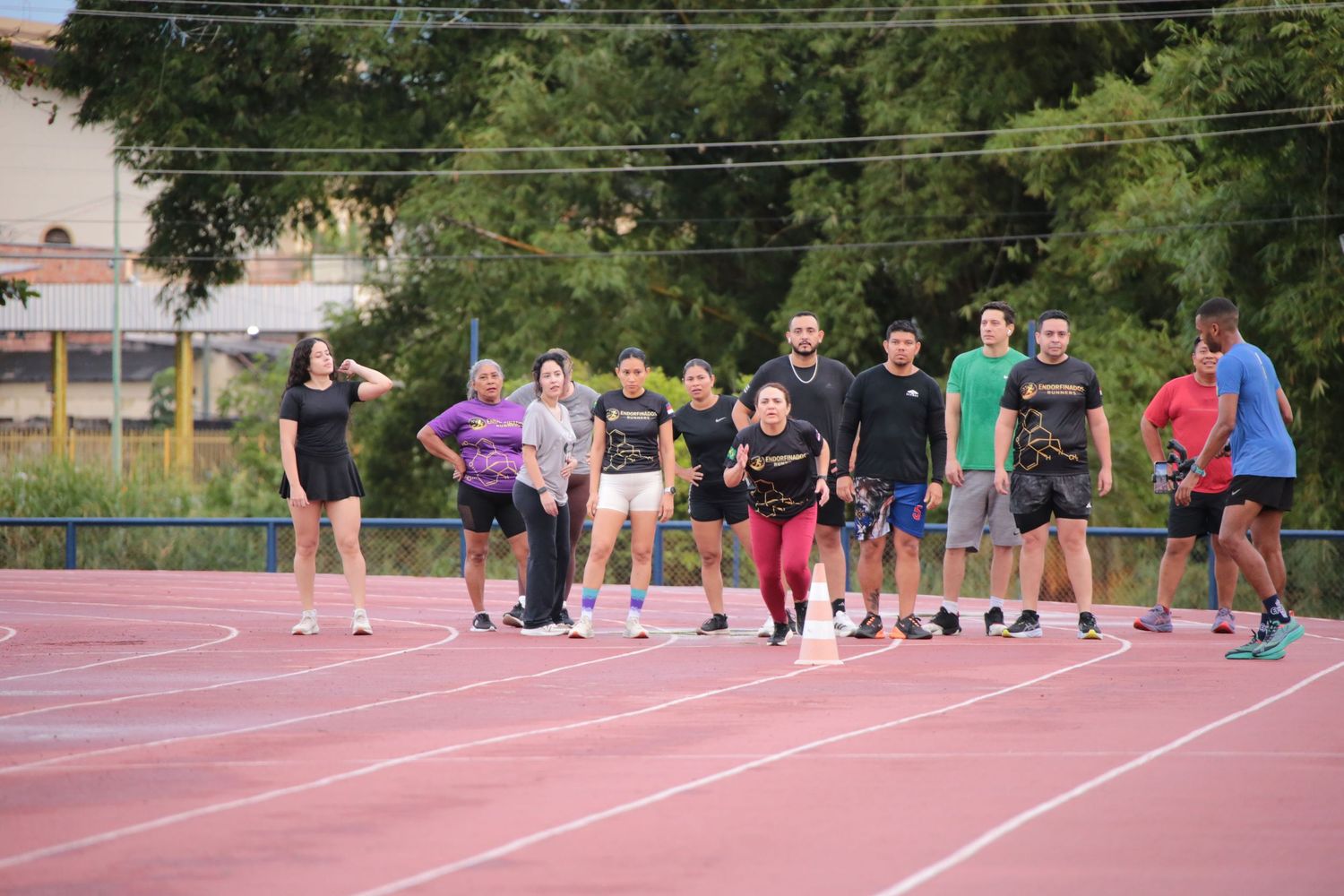 Diverse running group lines up on red athletic track during outdoor team training session.