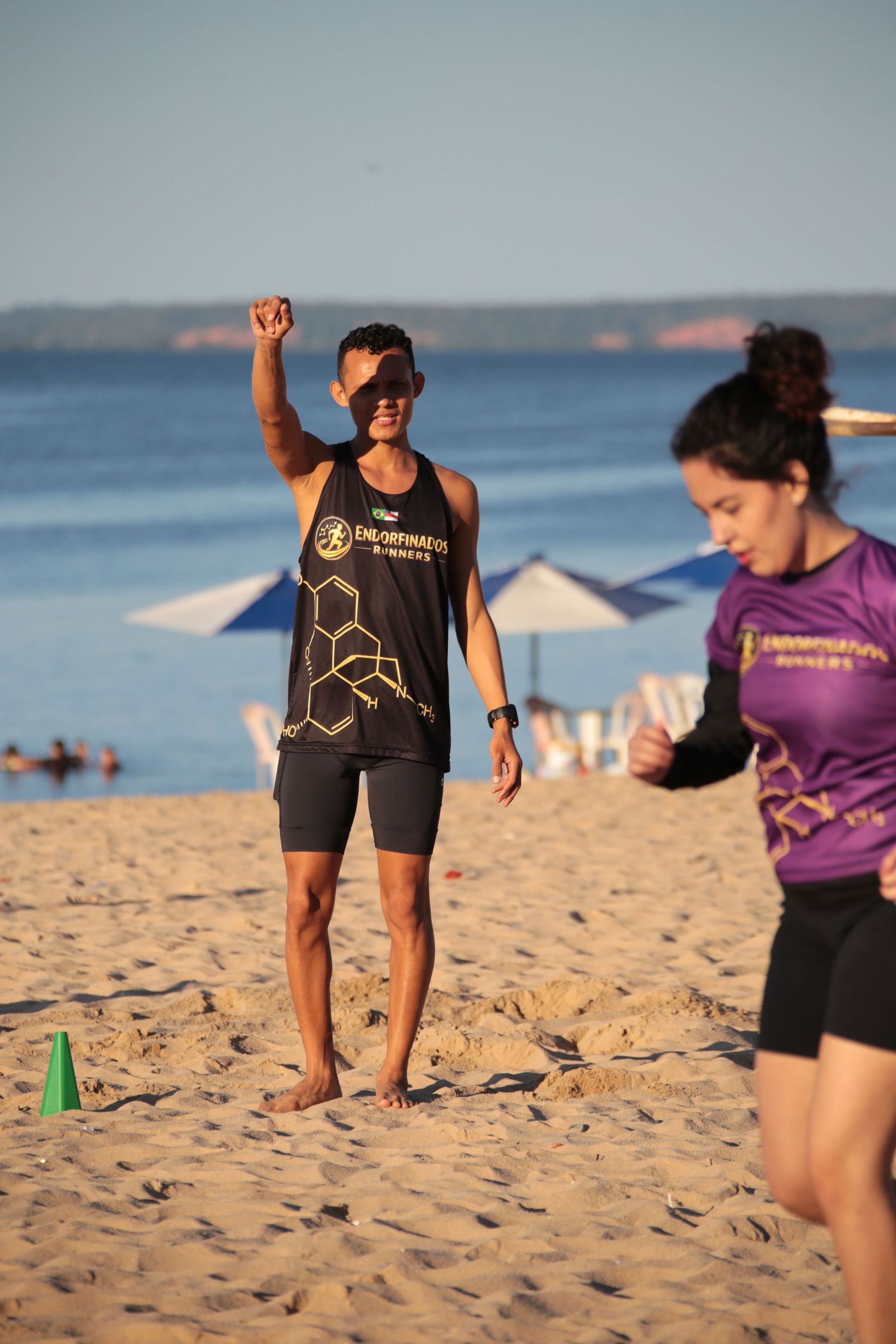 Male athlete in Endorfinados Runners tank top celebrating with raised fist on beach.