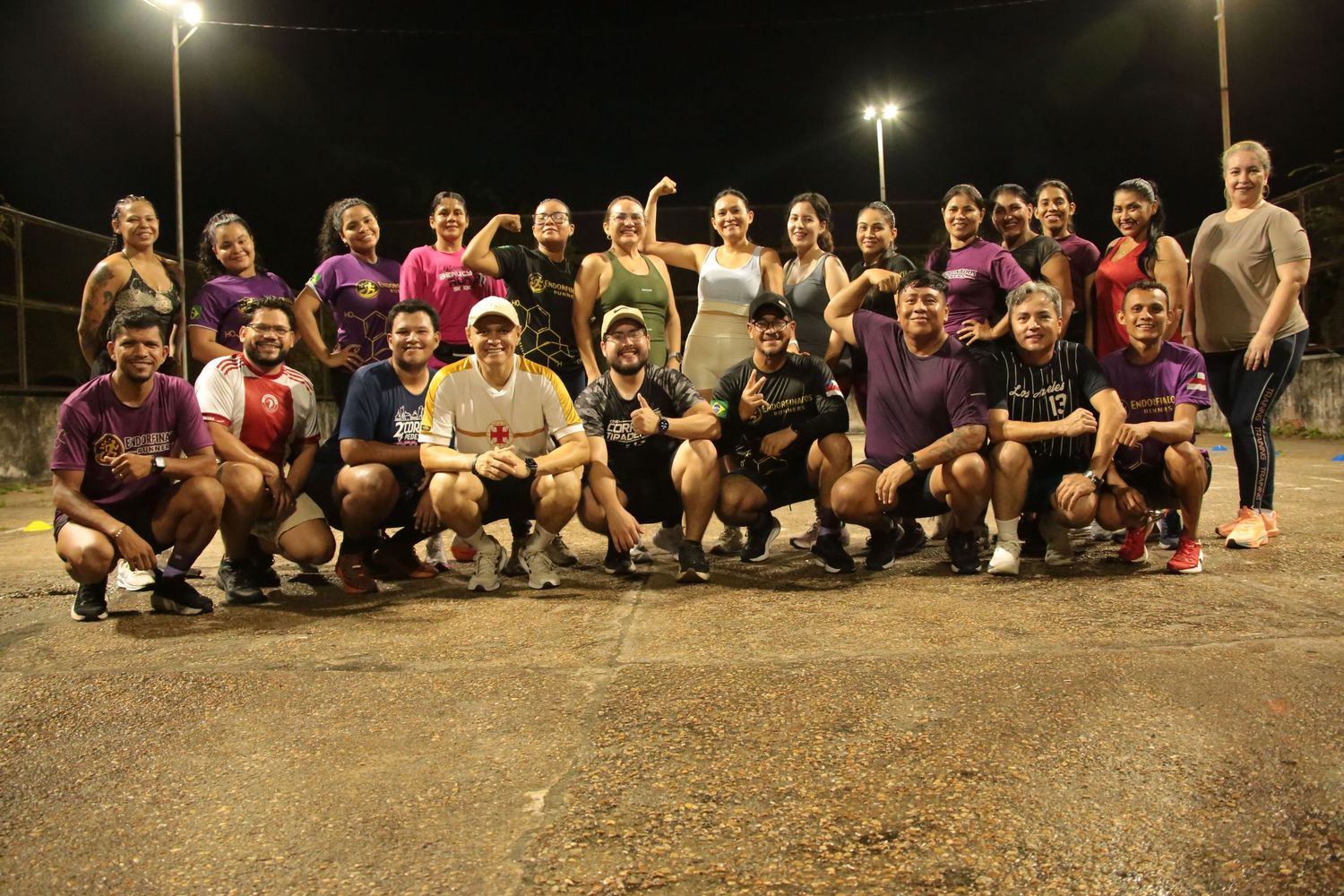 Large group of runners posing together for team photo on outdoor court under bright night lights.
