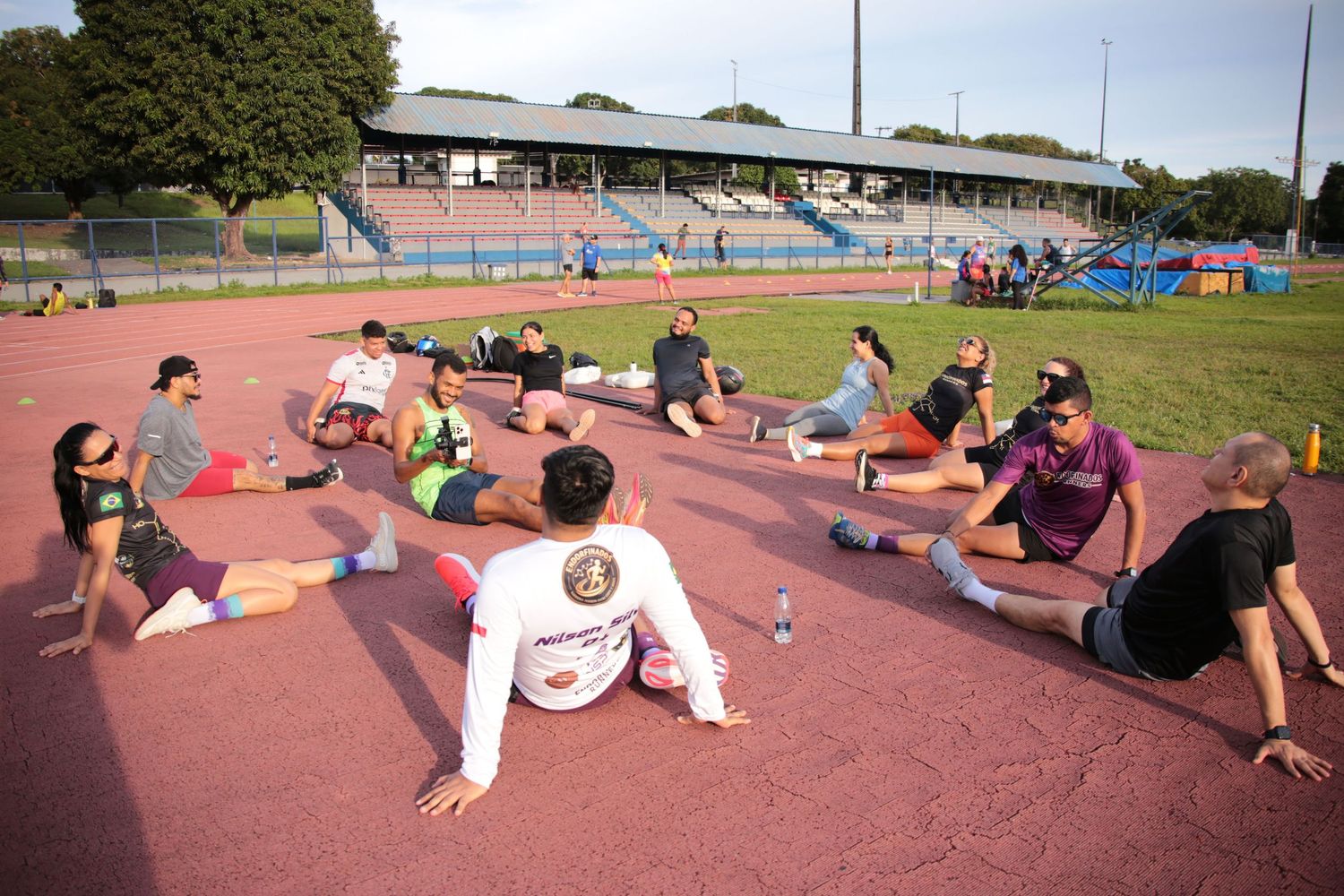 Athletes stretching in a circle on a red track at an outdoor stadium during a group training session.
