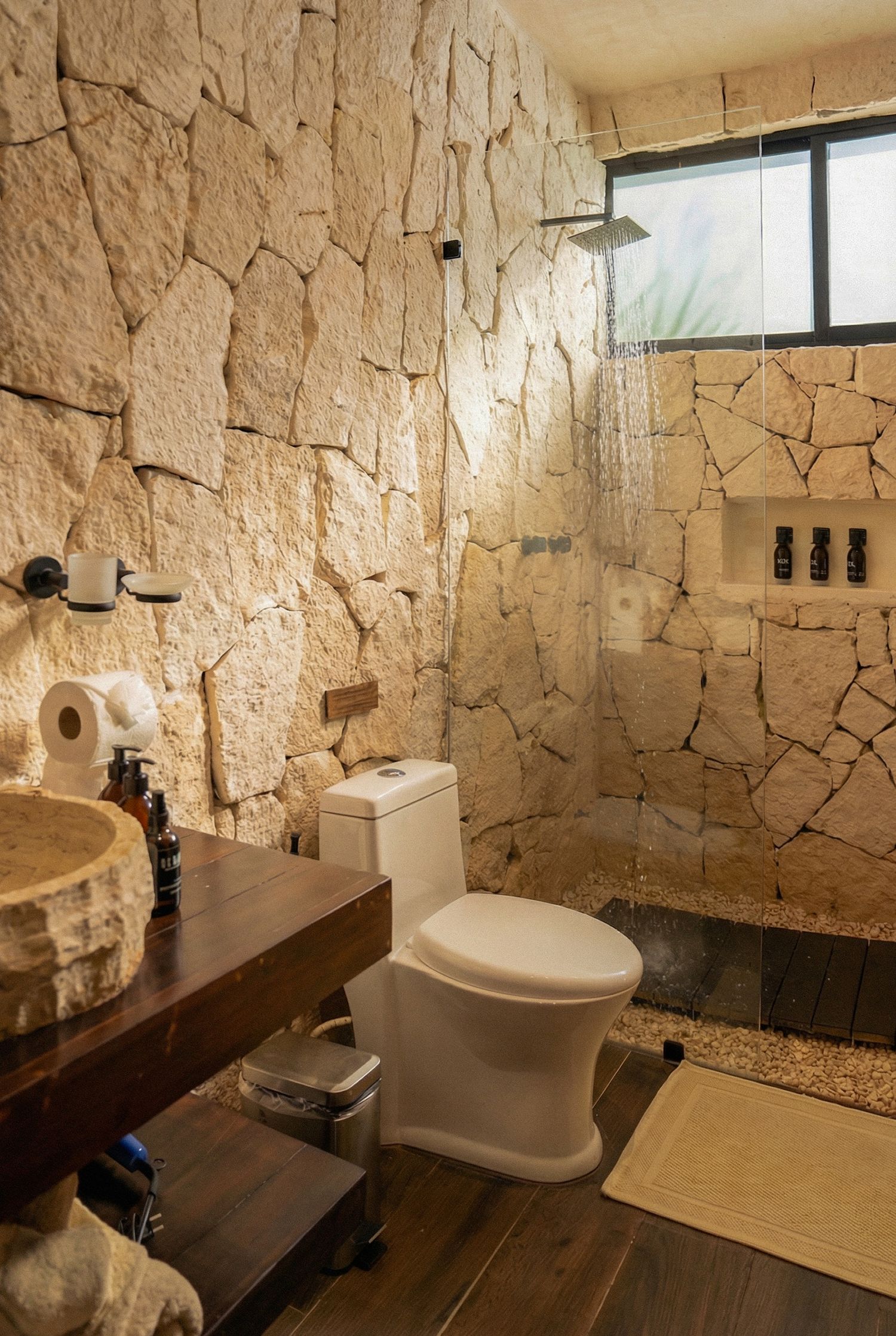 Rustic bathroom with natural stone walls, rain shower, wooden vanity and vessel sink in boutique hotel.