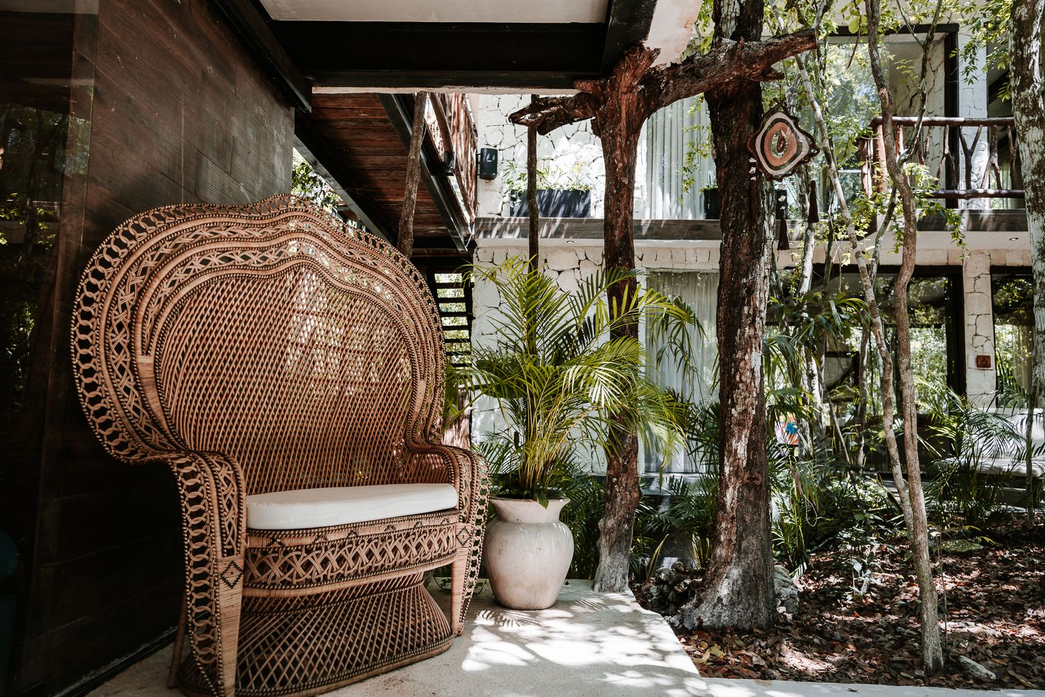Large woven rattan peacock chair on a shaded patio surrounded by lush tropical trees and plants.