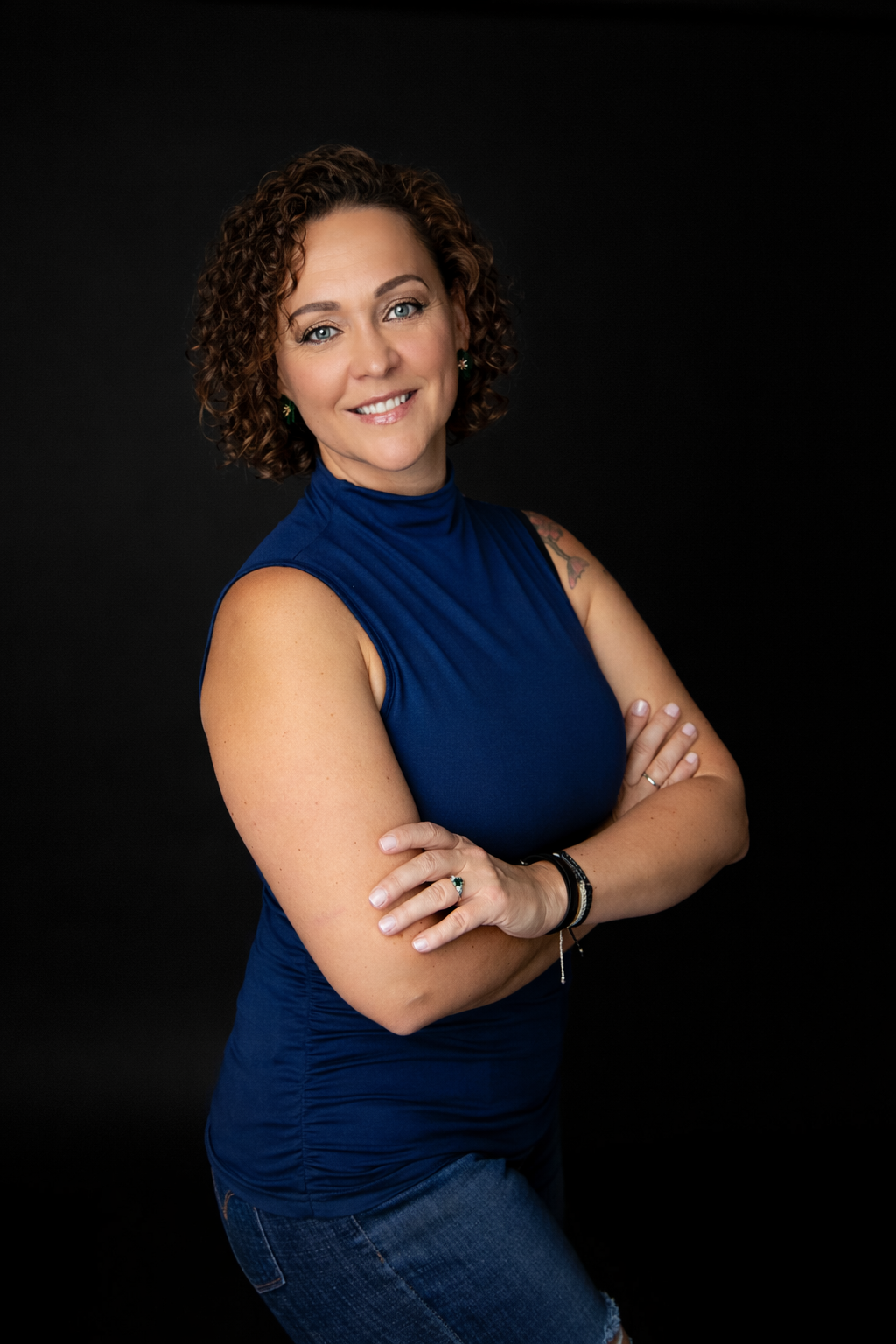 A person in a navy sleeveless top poses against a dark background in a professional portrait series.