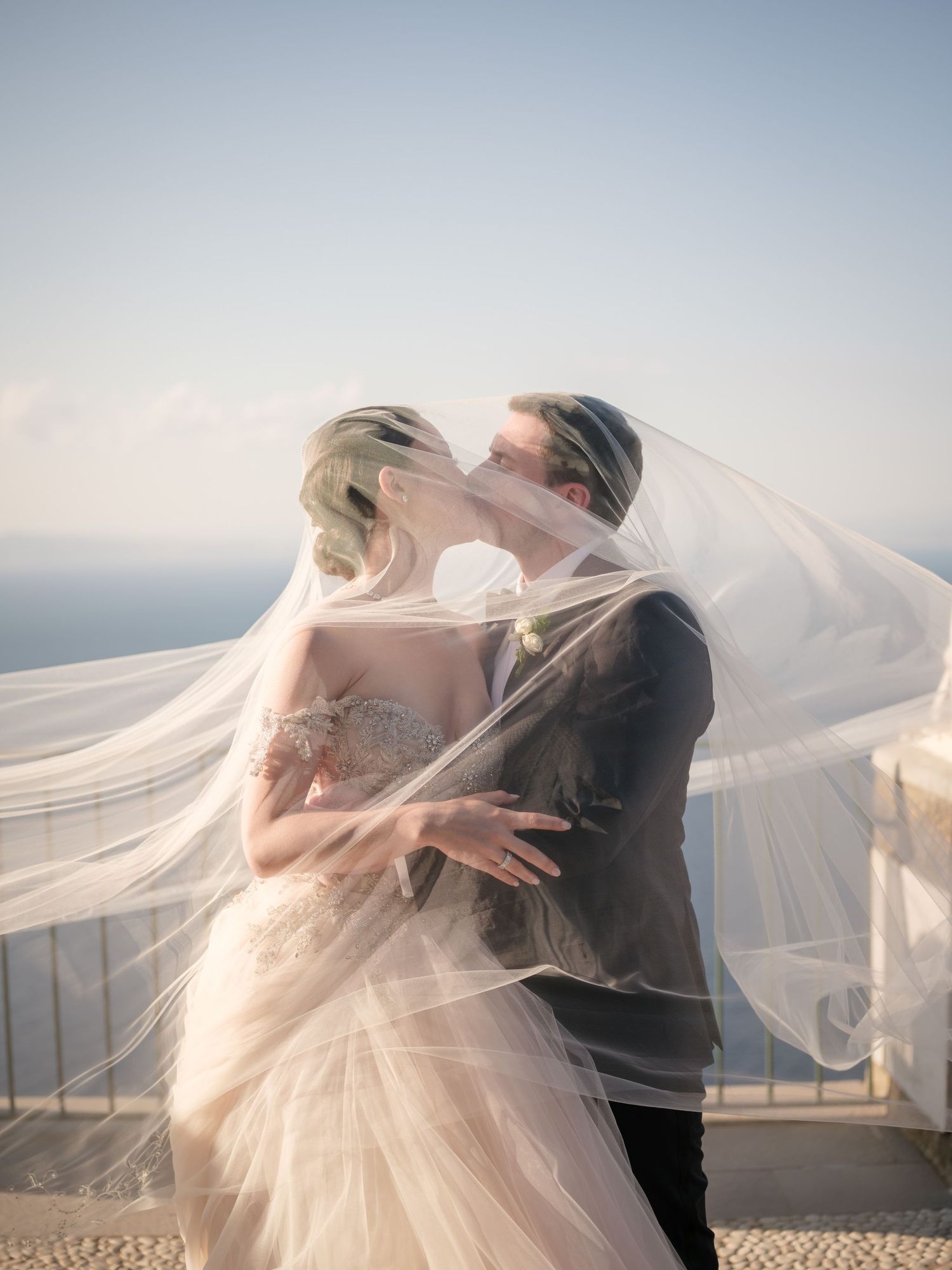 Romantic beach wedding portrait series showing couple dancing with flowing bridal veil billowing in the ocean breeze.
