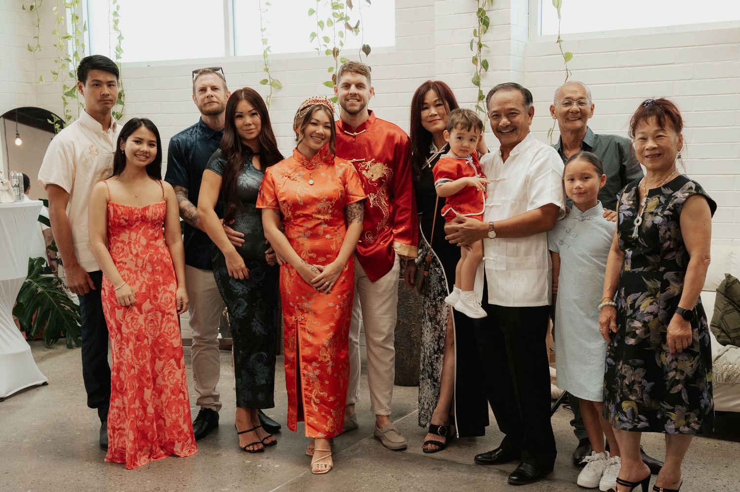 Family group photo at a Chinese wedding celebration with guests wearing traditional red qipao and formal attire.