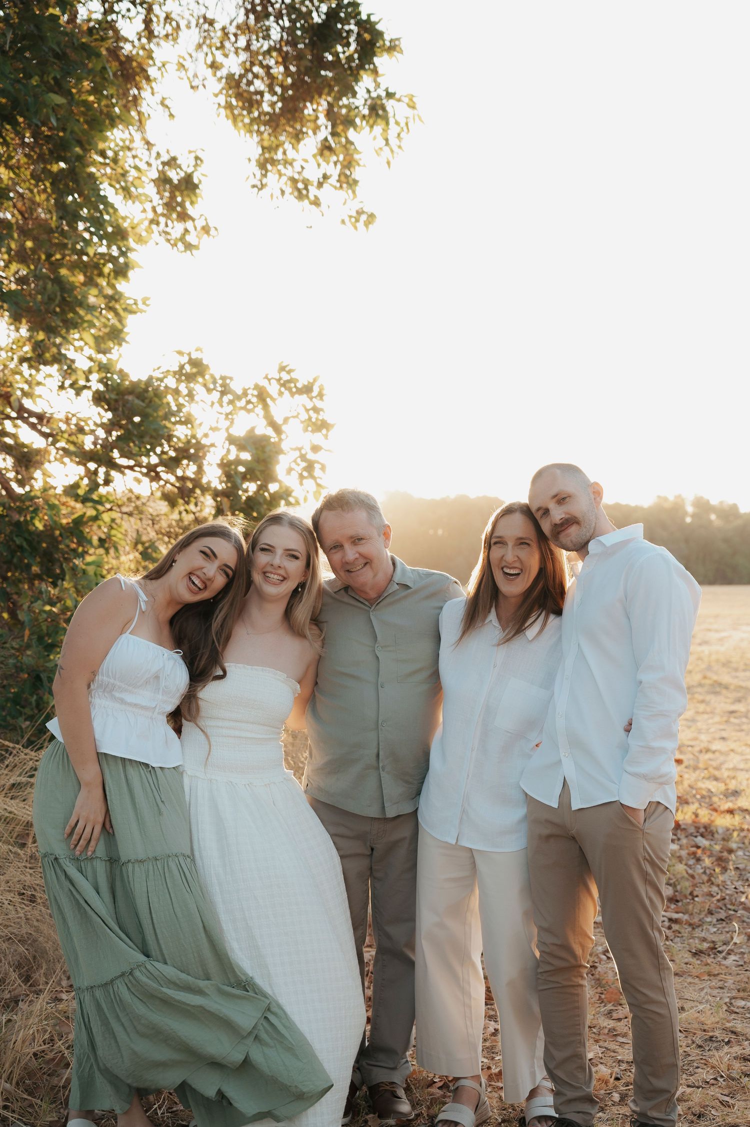 Five people posing together outdoors at golden hour, smiling in a sun-drenched field with warm backlight.