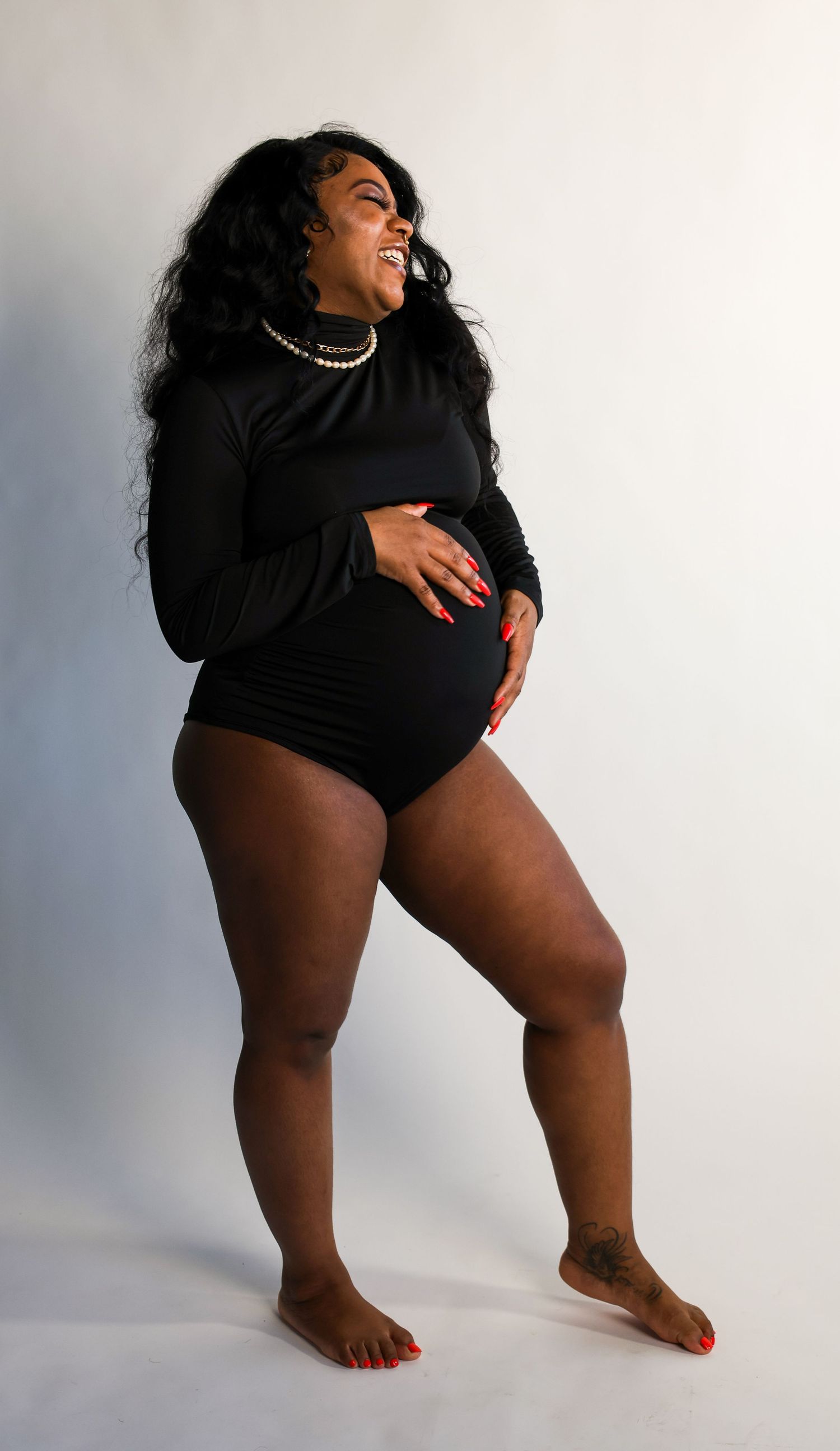 A joyful woman in a black bodysuit poses confidently against a light background during a studio photoshoot.