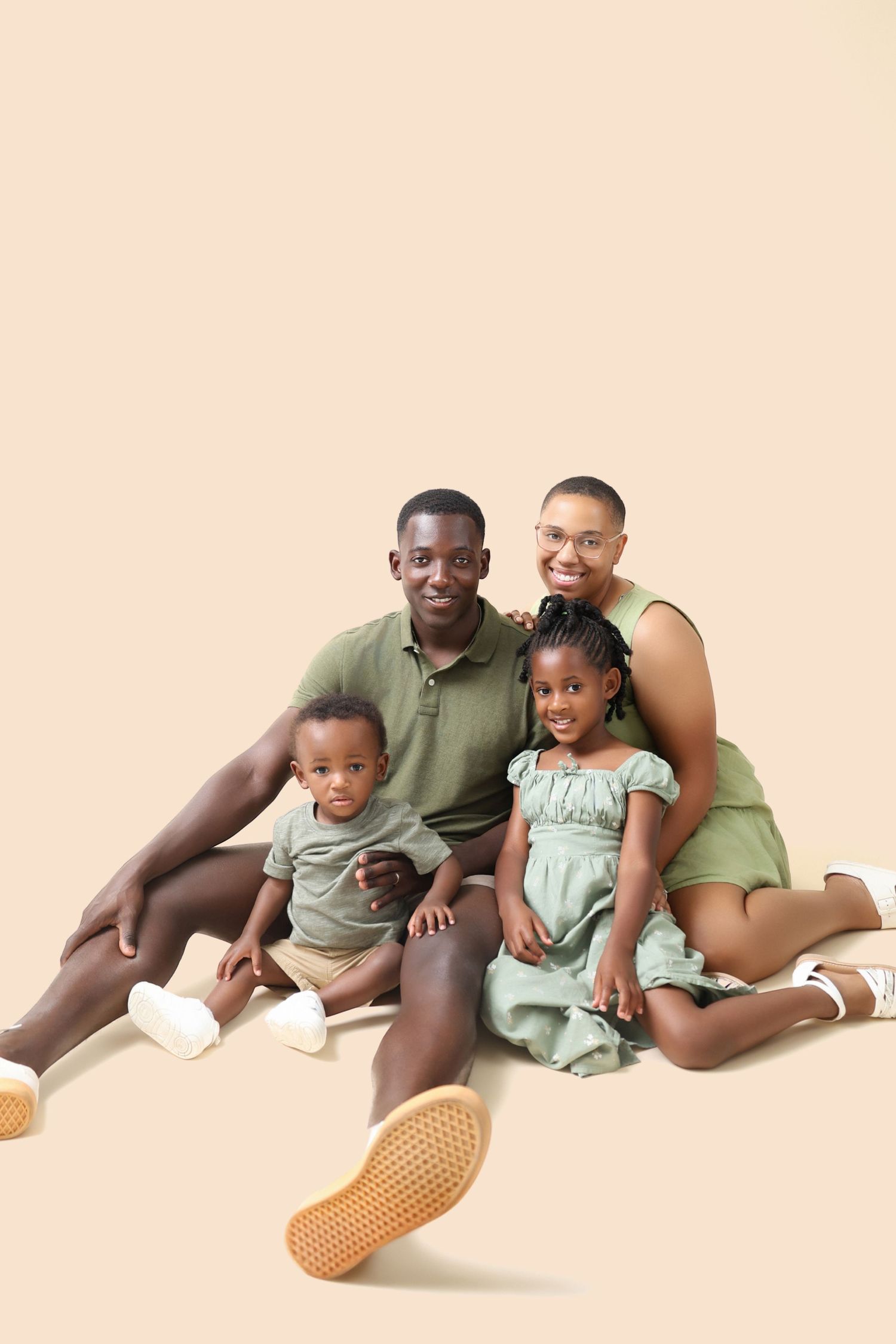 Family wearing coordinated casual outfits in green and tan sitting together against peachy beige background.