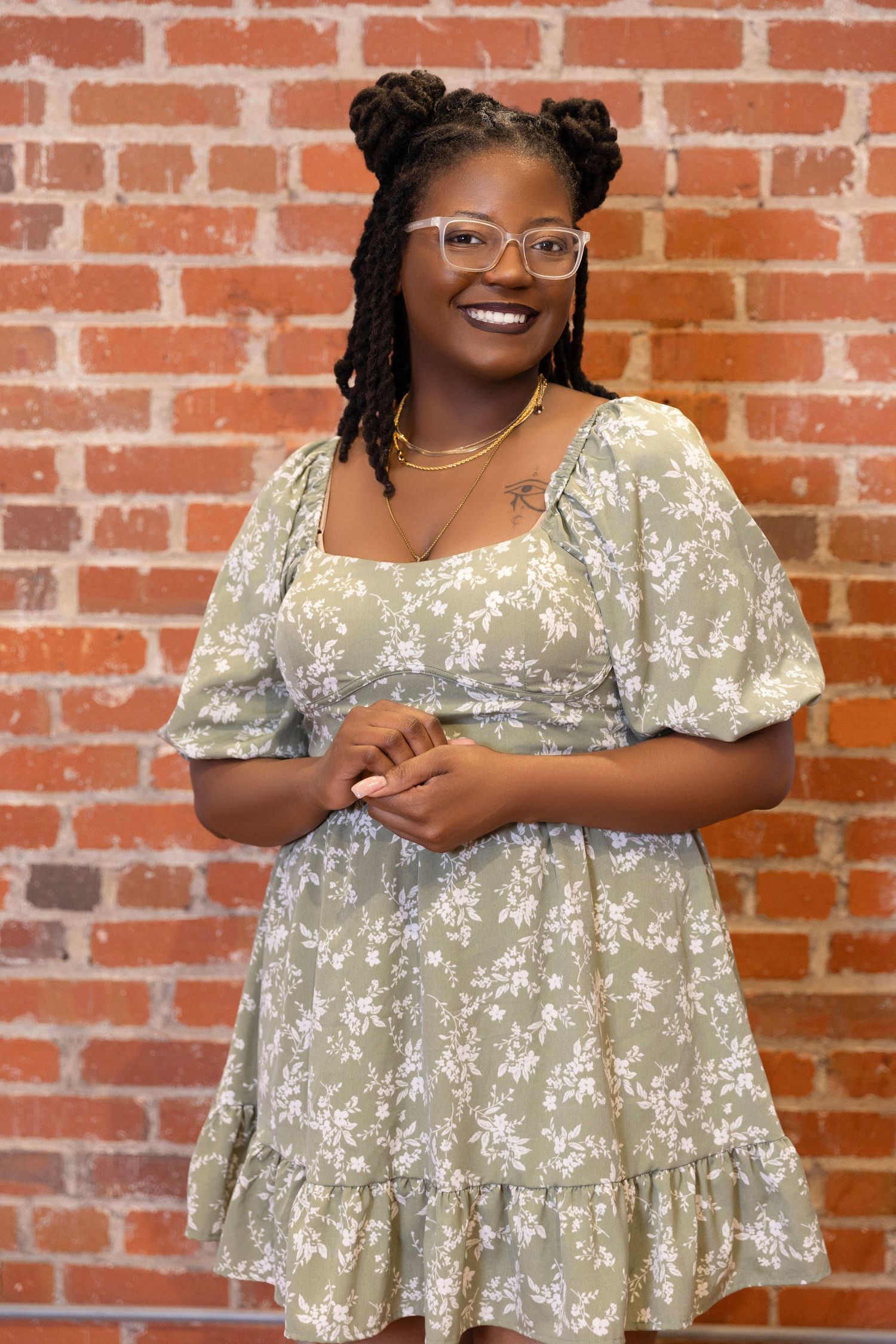 Portrait against brick wall wearing floral dress and glasses with styled hair.
