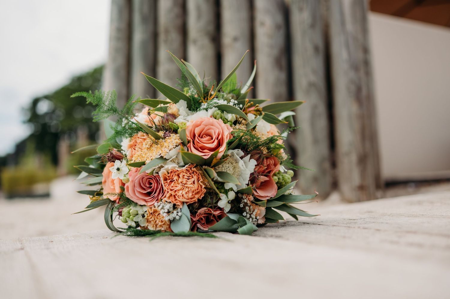 A romantic floral arrangement with peach roses, sage greenery and blush blooms adorns a rustic wooden surface.