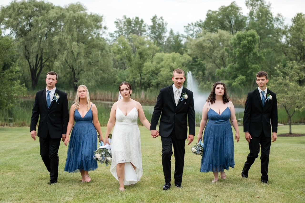 Wedding party walks across green lawn with bridesmaids in blue dresses.