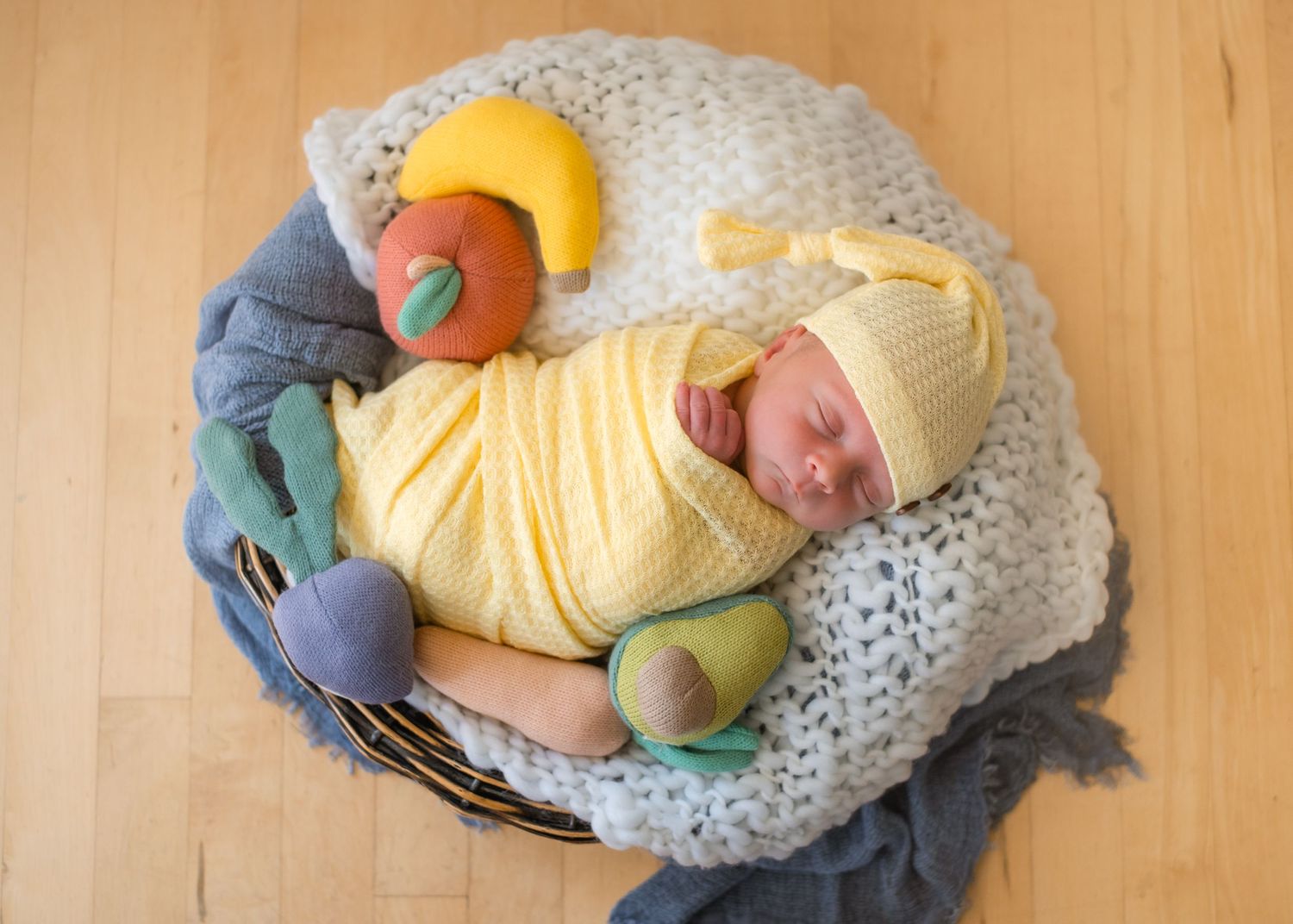 Sleeping newborn wrapped in yellow swaddle surrounded by plush fruit toys.