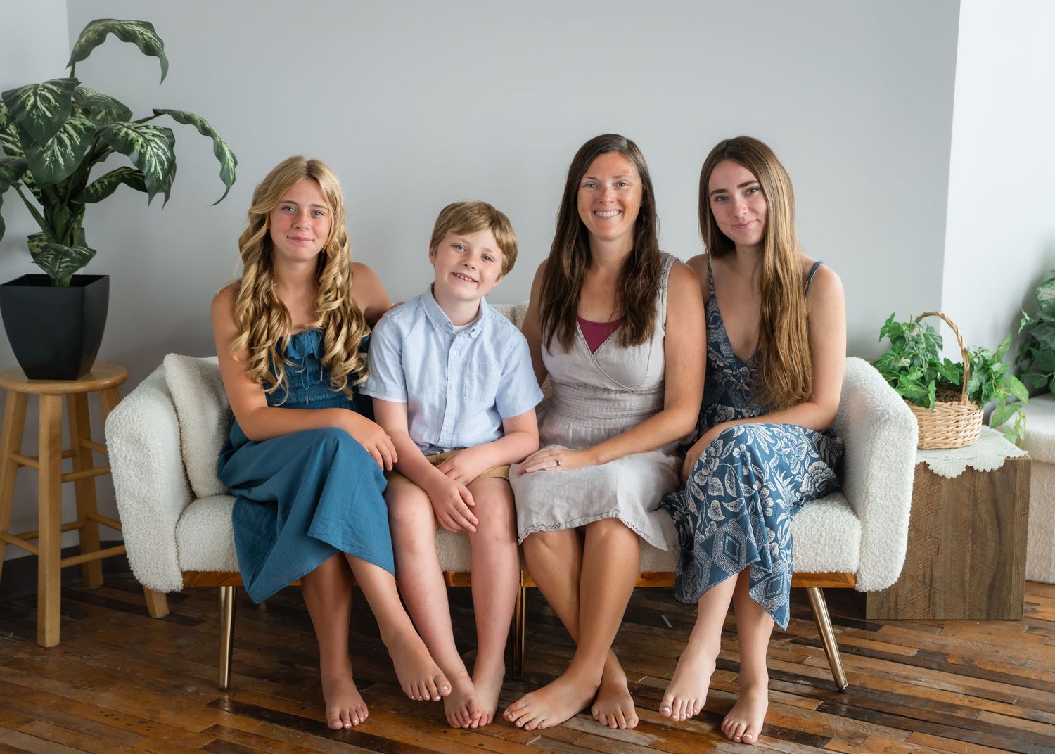 A woman and three children sit together smiling on a white bench in a bright modern room with wood floors.