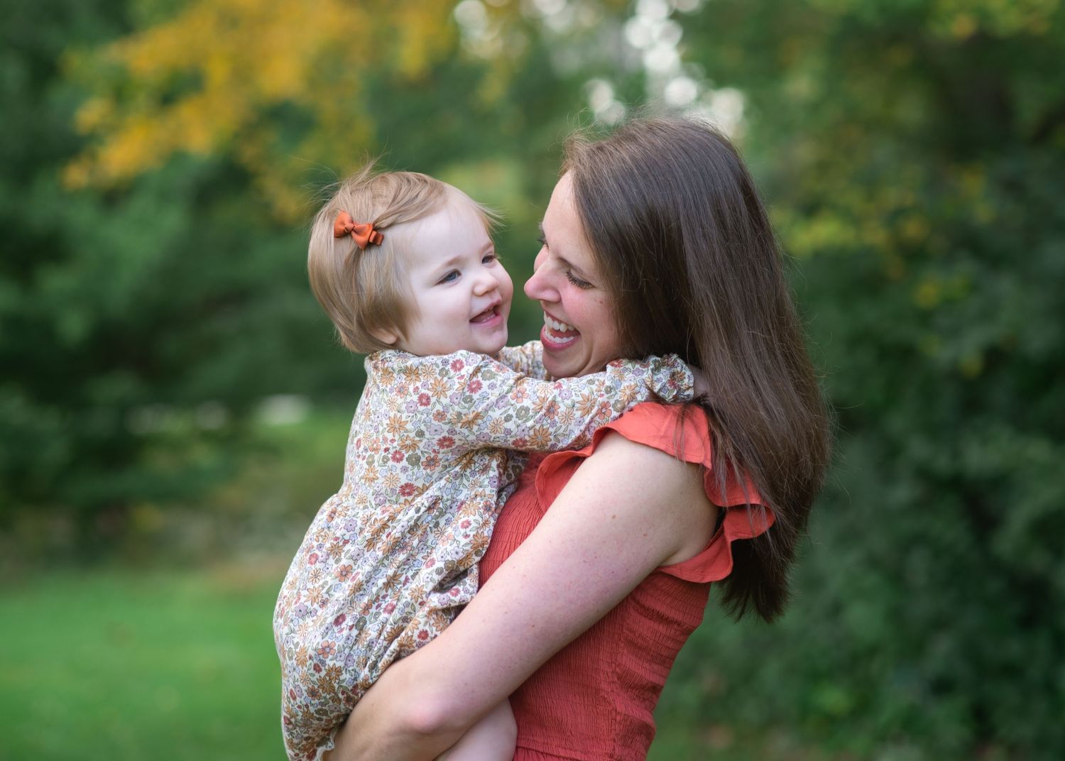 Mother and child share laughter during an intimate outdoor portrait session with golden fall scenery.