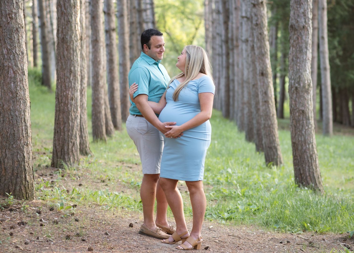 Couple embracing on forest path during outdoor maternity photo session.