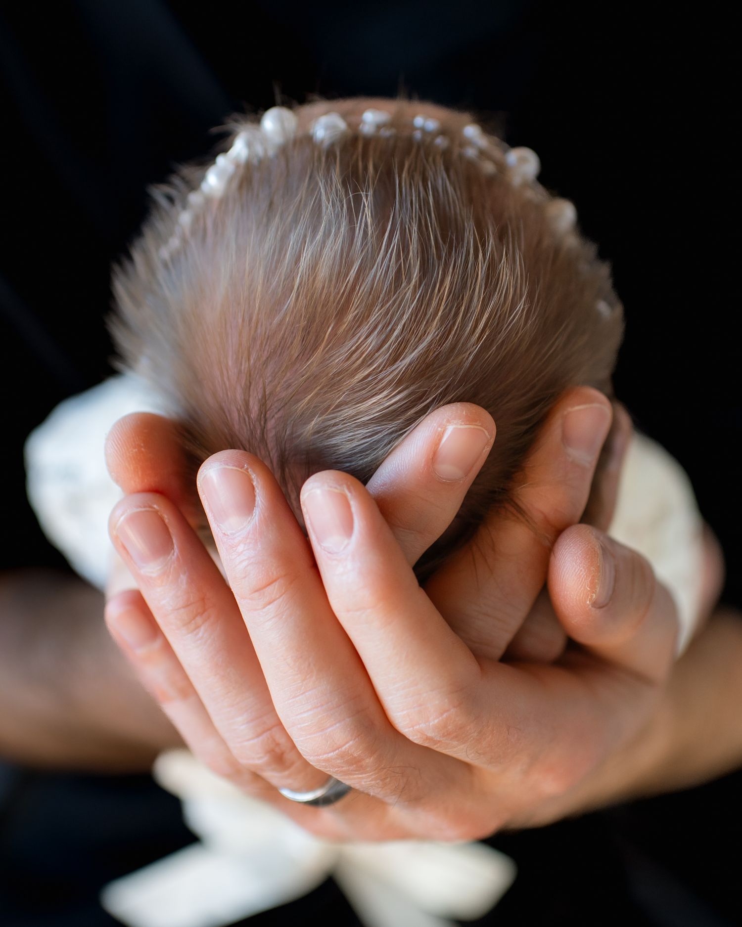 Close-up of tiny newborn baby's head cradled gently in parent's hands.