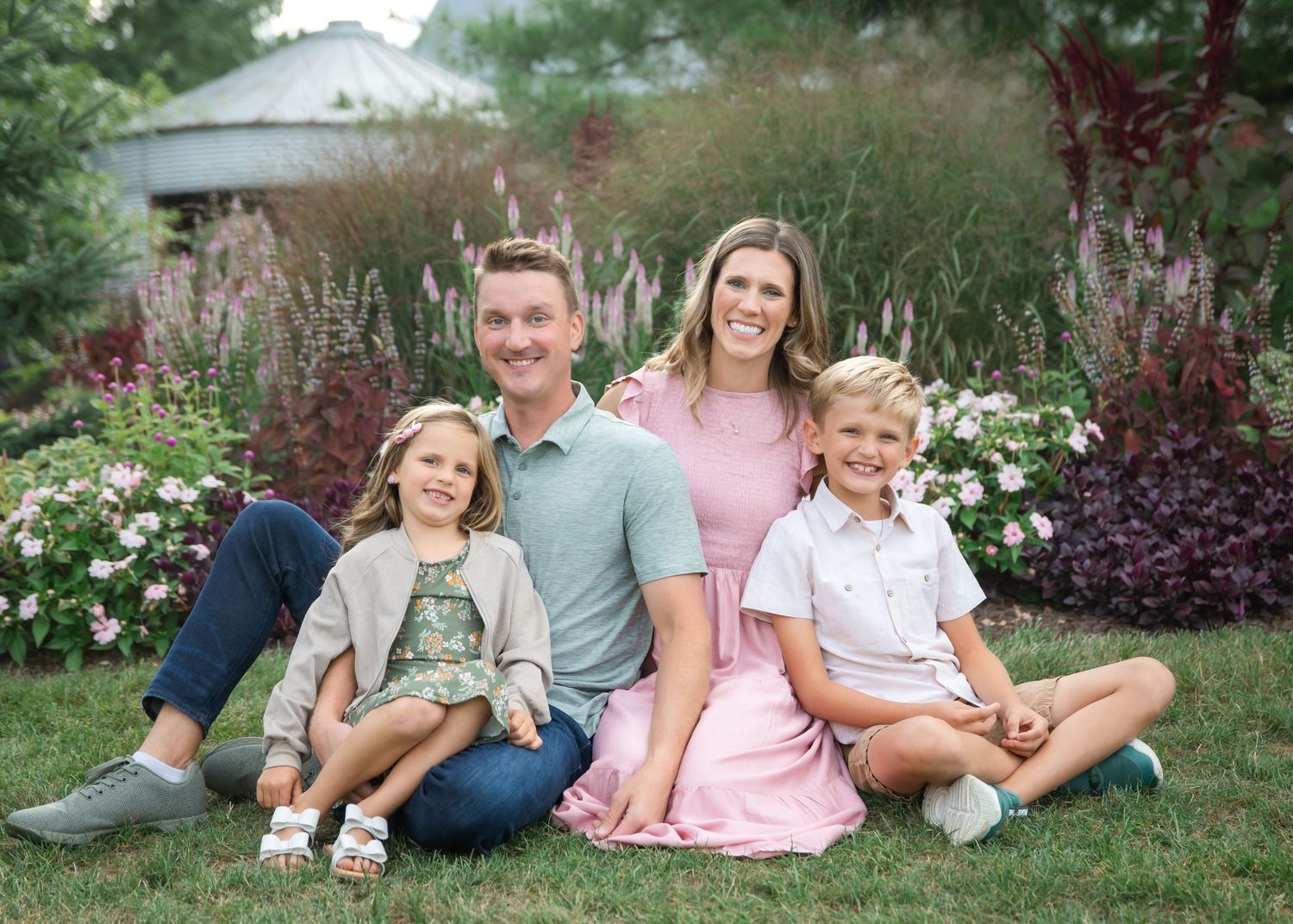 Happy family of four smiling together outdoors in a lush garden with colorful flowers in bloom.