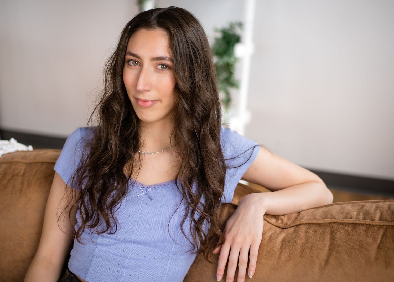 Woman in purple shirt relaxes on brown leather couch in bright living room.