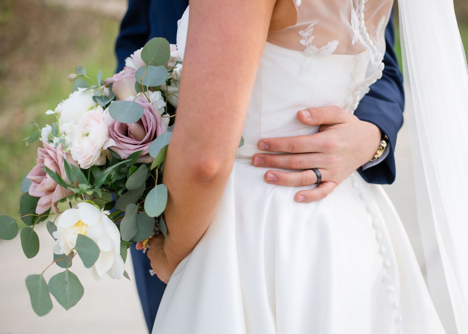 A wedding couple embraces while holding a romantic bouquet of pink and white flowers with eucalyptus.