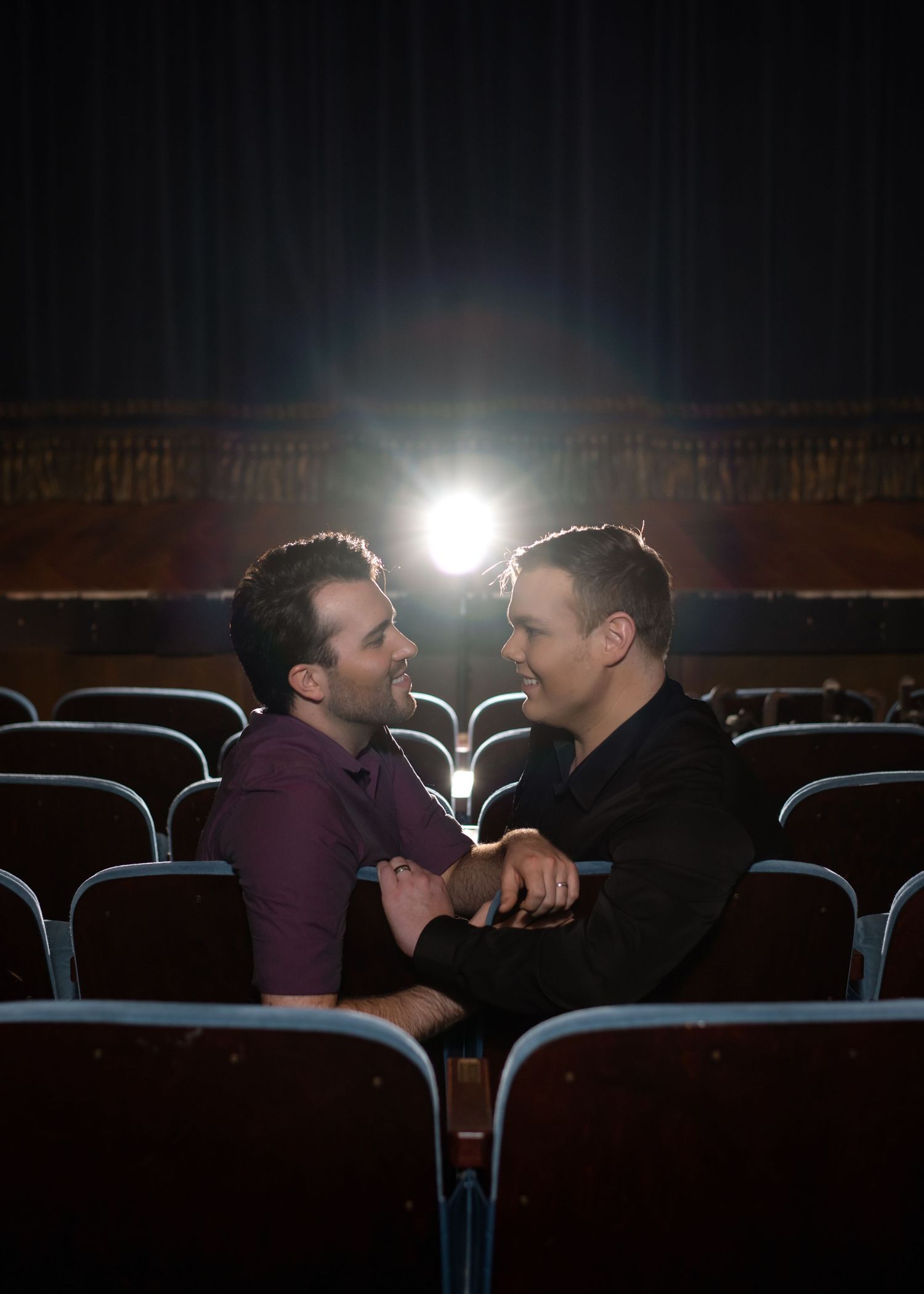 A couple shares an intimate moment in theater seats with dramatic backlighting.