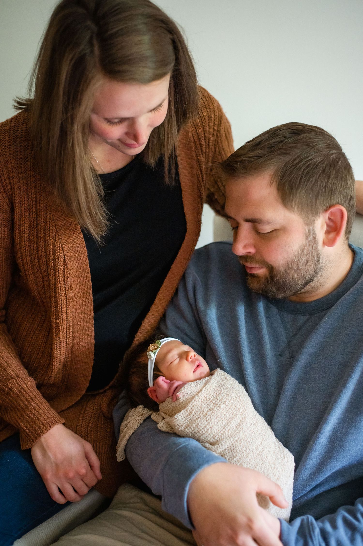 A tender moment as parents gaze lovingly at their swaddled newborn baby resting in their arms.