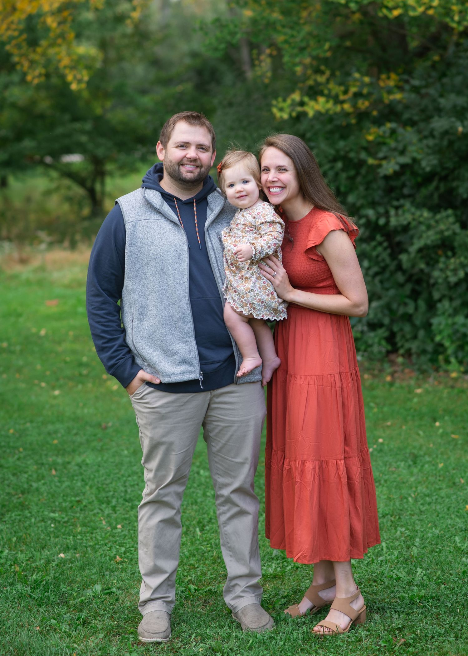 Outdoor family portrait with parents and baby against lush greenery wearing coordinated casual attire.