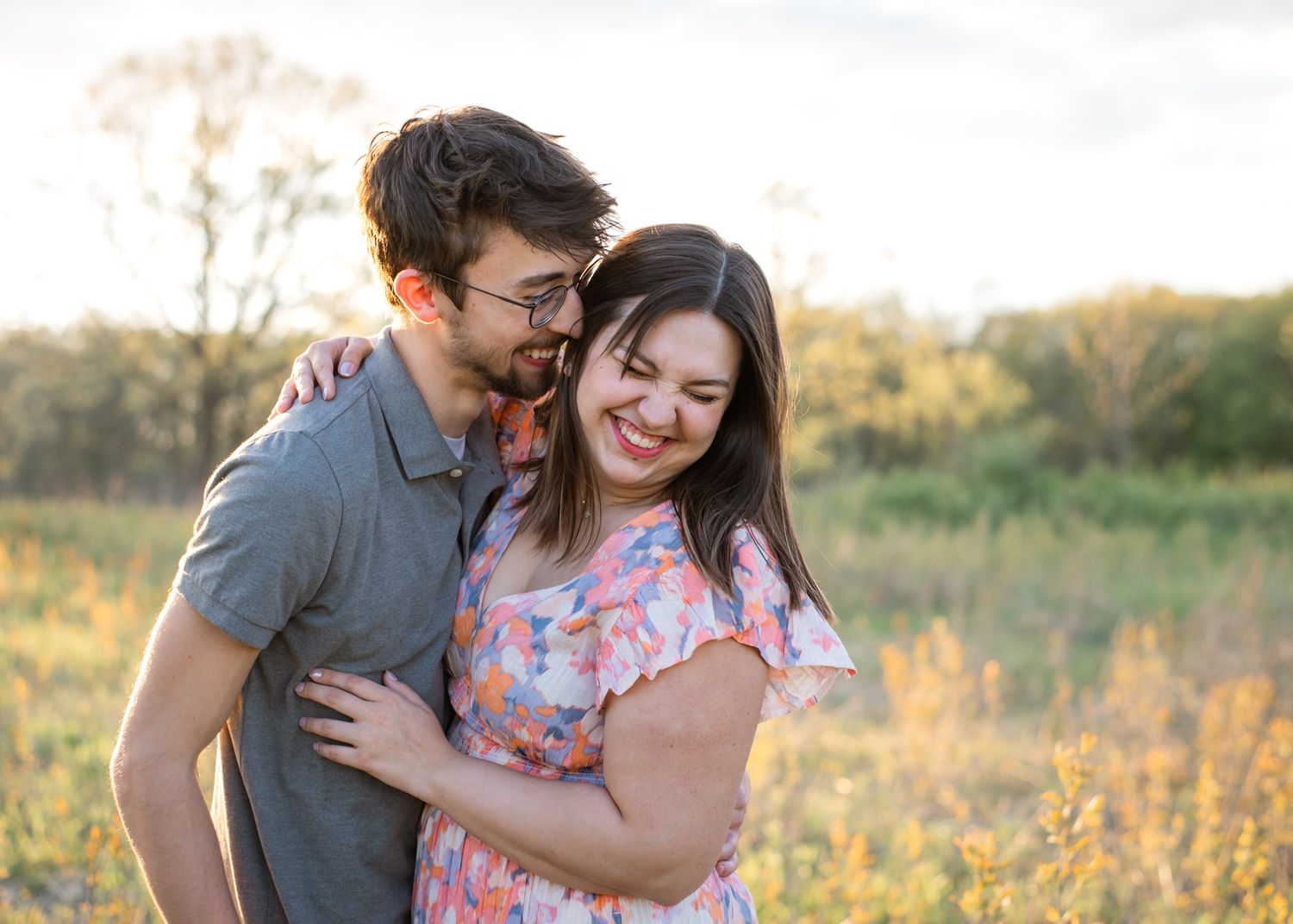 Loving couple embraces and laughs together in a golden sunlit field.