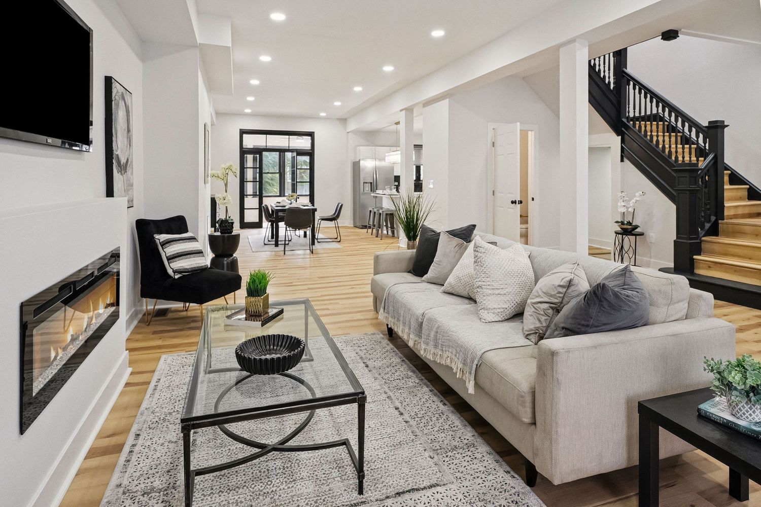 Modern open concept living room features white walls, gray sofa, and black staircase with contemporary decor.