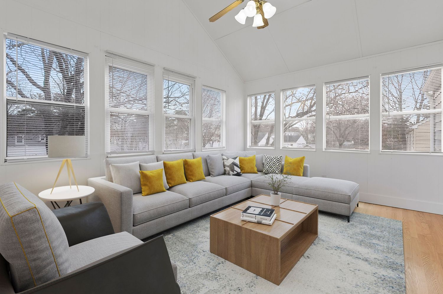 Modern sunroom with white walls, gray seating, and yellow accent pillows features large windows and natural light.