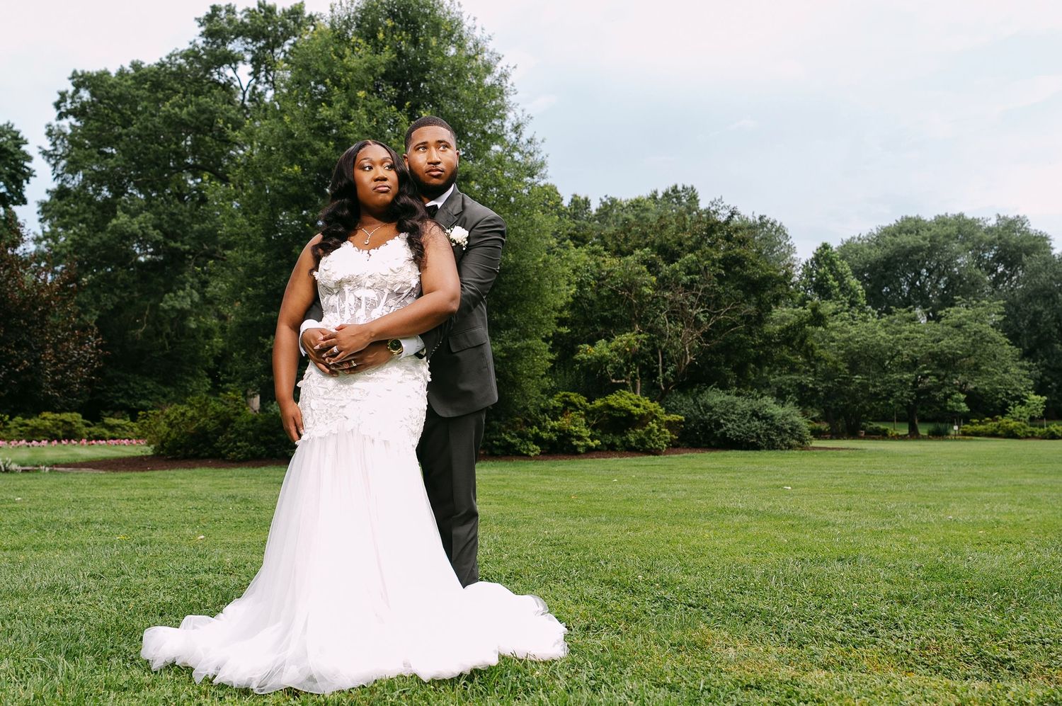 Bride in white gown and groom in gray suit pose together on green lawn right after Baltimore County courthouse wedding