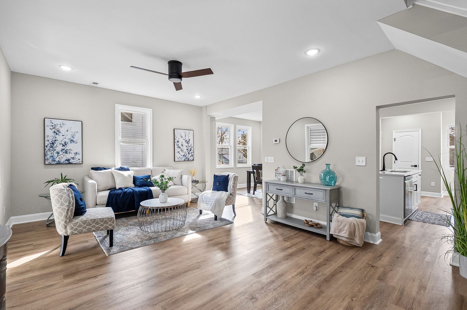 Modern living room with gray sectional sofa, white walls, hardwood floors and contemporary ceiling fan.