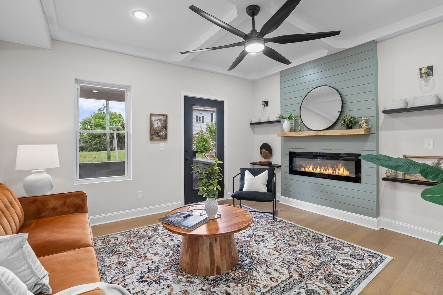 Modern living room features a tan leather accent chair, ceiling fan, and built-in fireplace with gray and white decor.