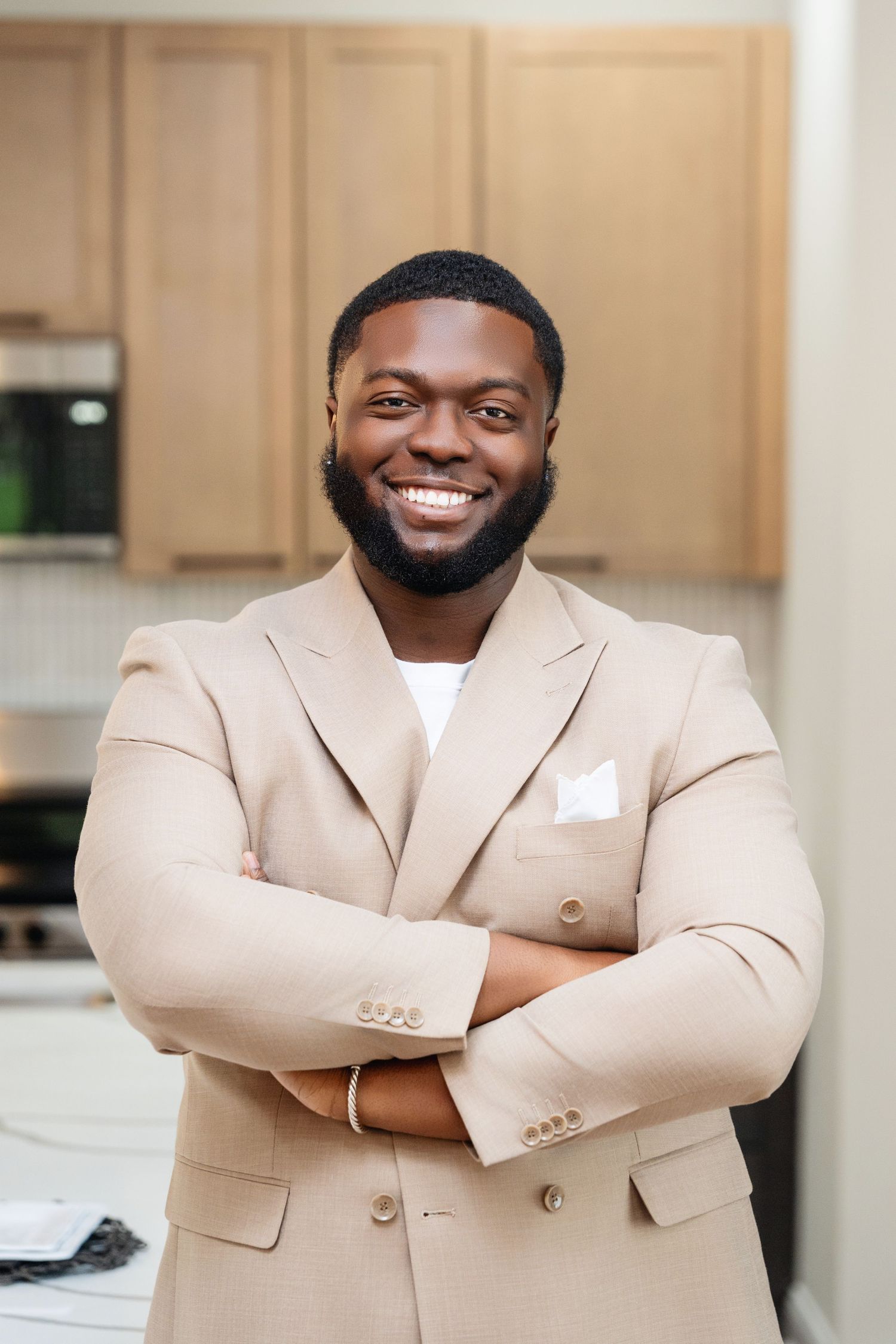 Professional wearing a cream double-breasted suit jacket stands with crossed arms in a kitchen setting.