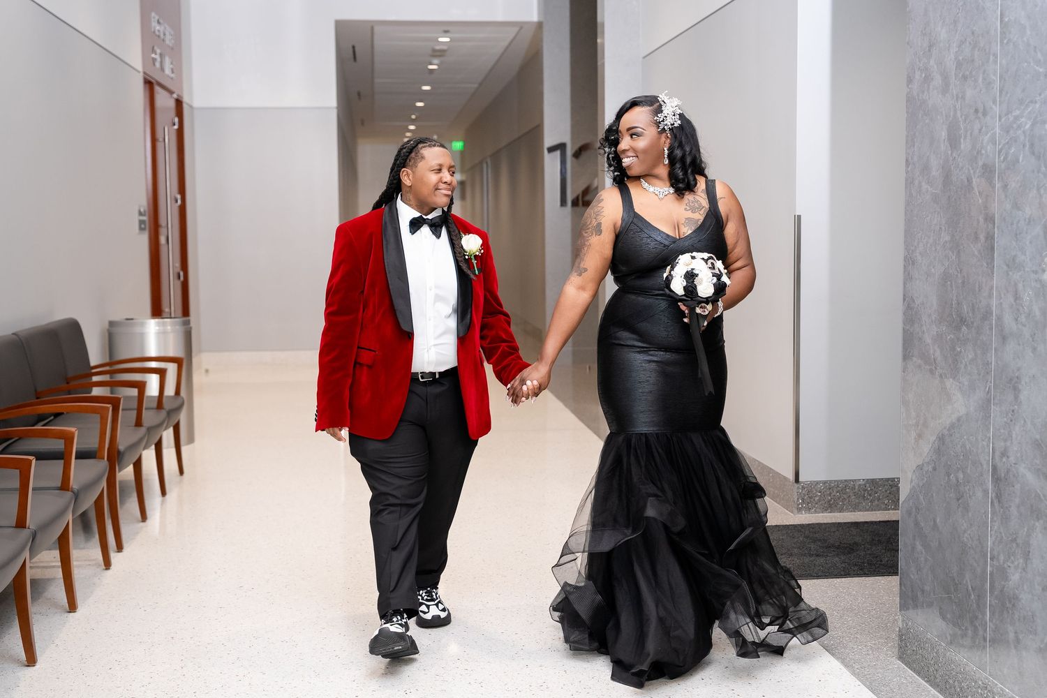 Two women in elegant formalwear, one in a red blazer and one in a black gown for wedding at Howard County Maryland Court house.