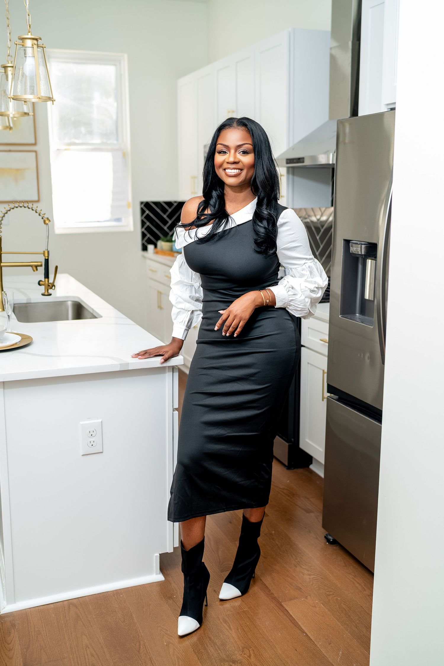 Professional standing in modern kitchen wearing black dress with white sleeves and stylish black and white boots.