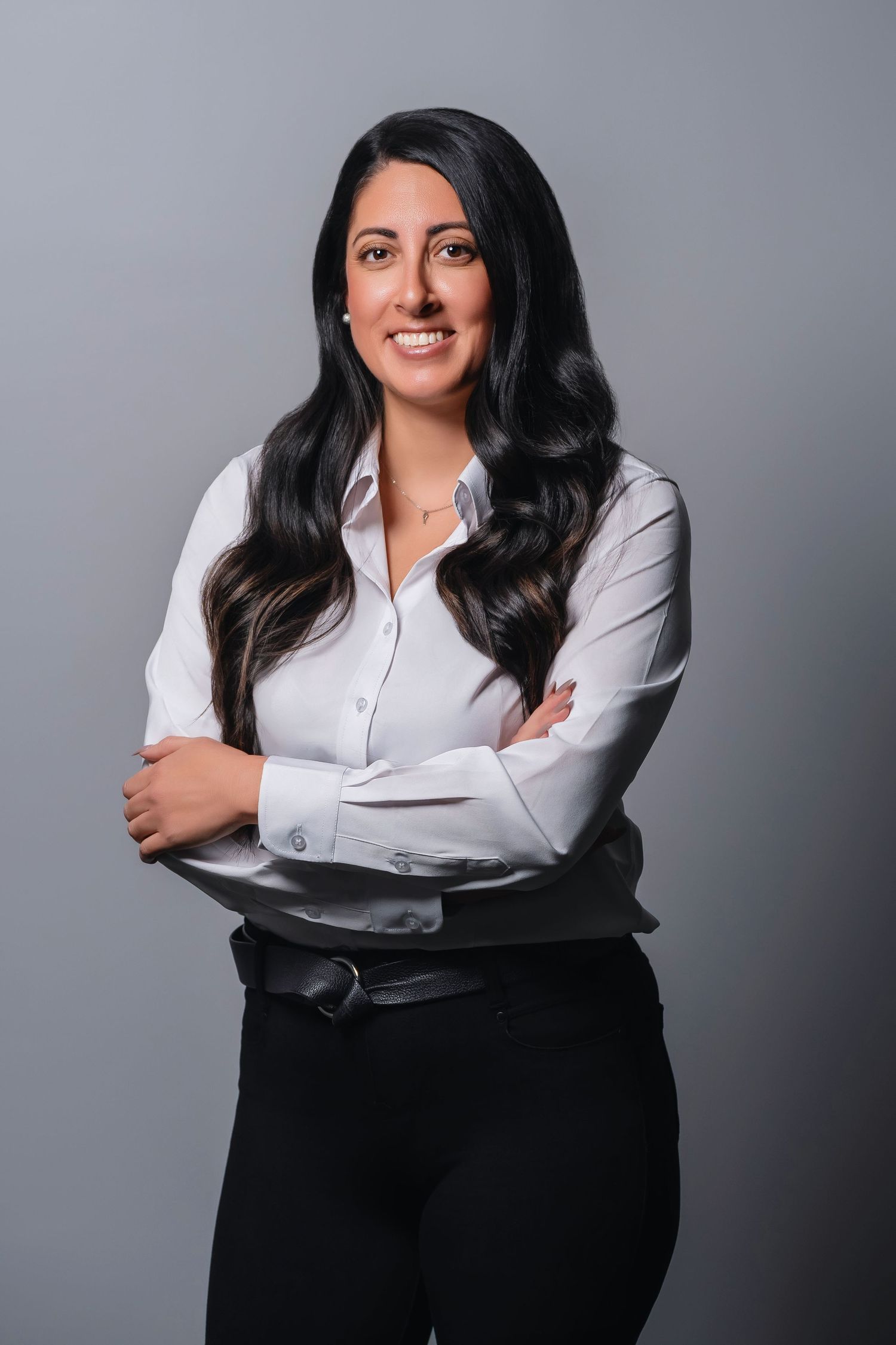 Professional in white button-down shirt and black pants poses with crossed arms.