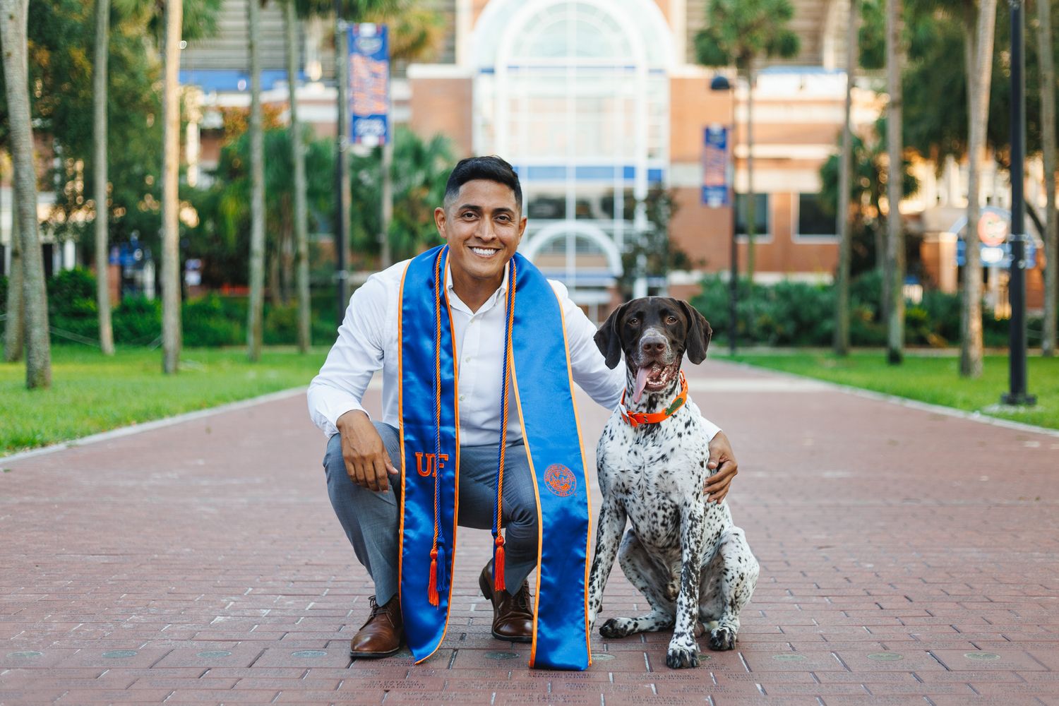 Photo of man wearing white dress shirt, grey dress pants, and a blue and orange UF graduation stole with his arm around