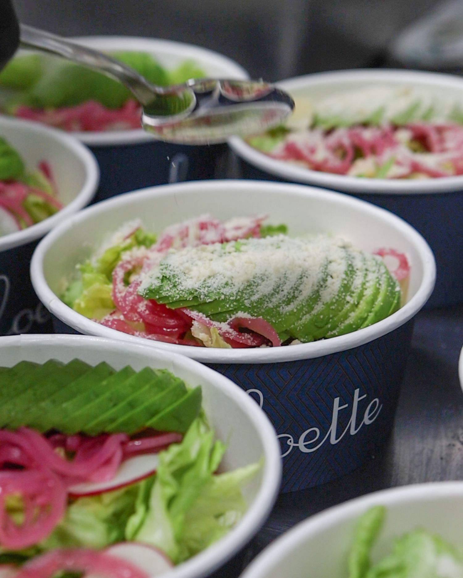 Multiple plates of Caesar salads garnished with pickled red onions and parmesan cheese arranged in a row.