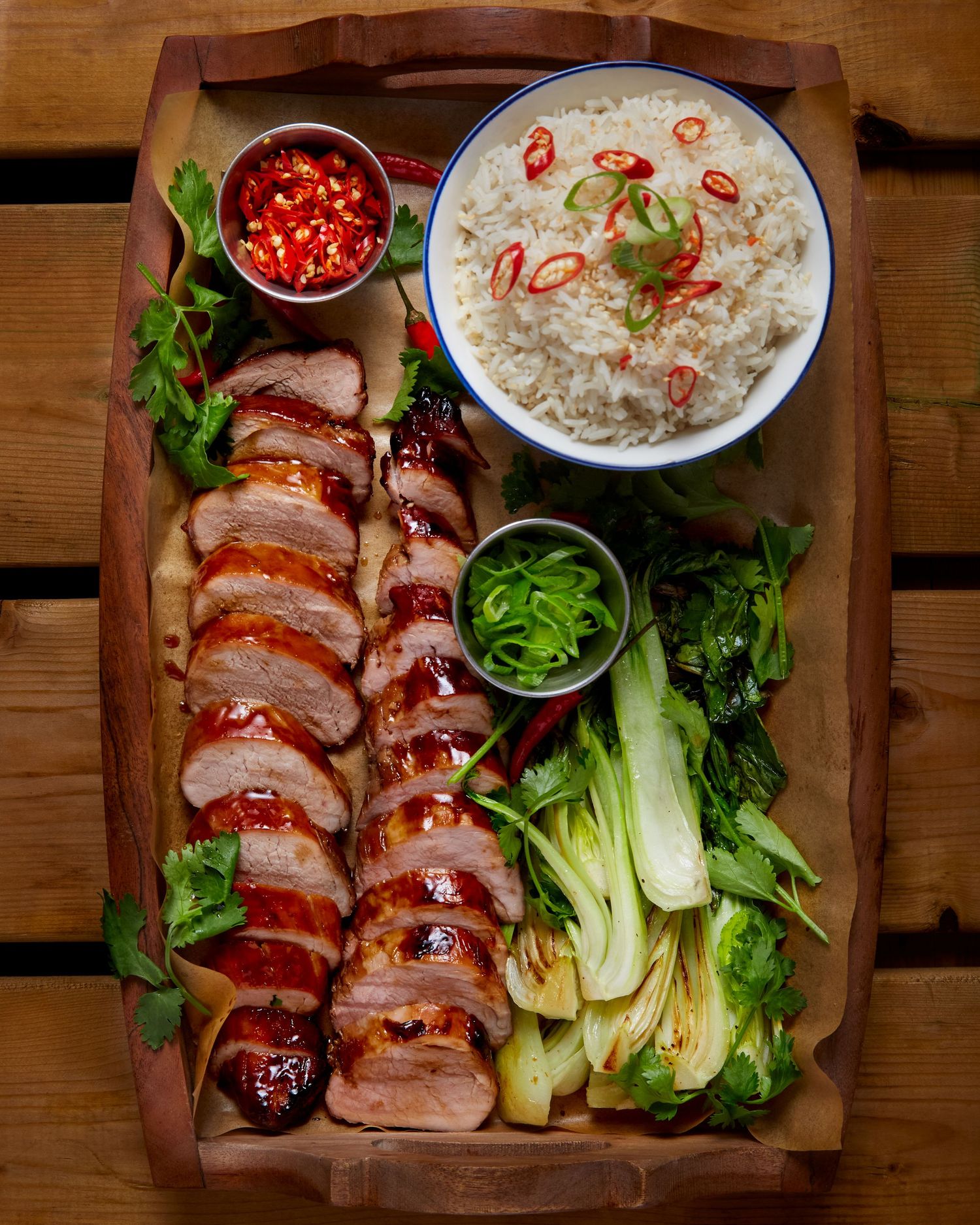 Plated pork tenderloin slices with grilled baby bok choy and creamy dipping sauce on a rustic wooden board.