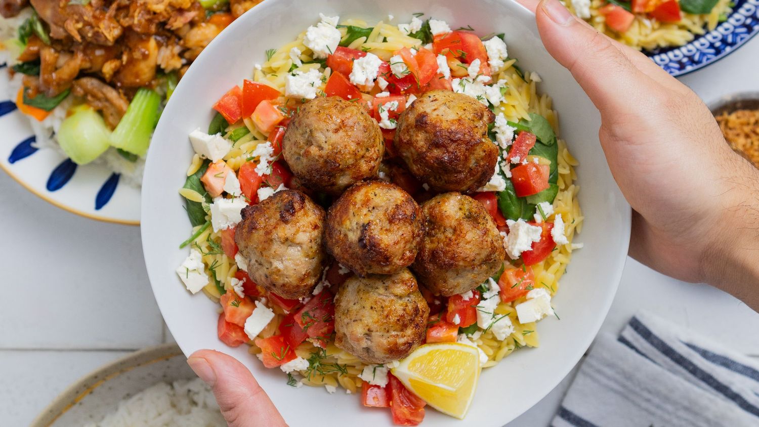 Overhead view of Greek meatballs served on a bed of colorful Mediterranean salad with feta cheese and lemon wedge.