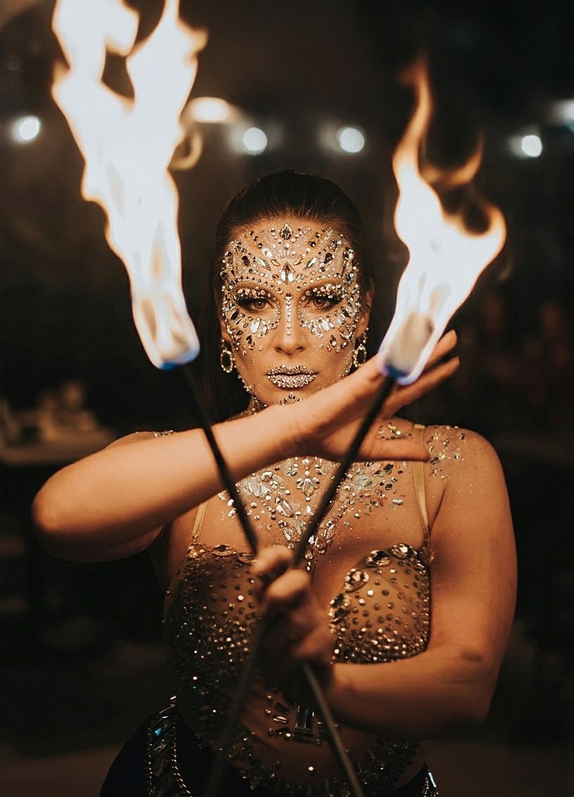 Fire dancer performs with flames against dark background creating dramatic light effects and sparkles.
