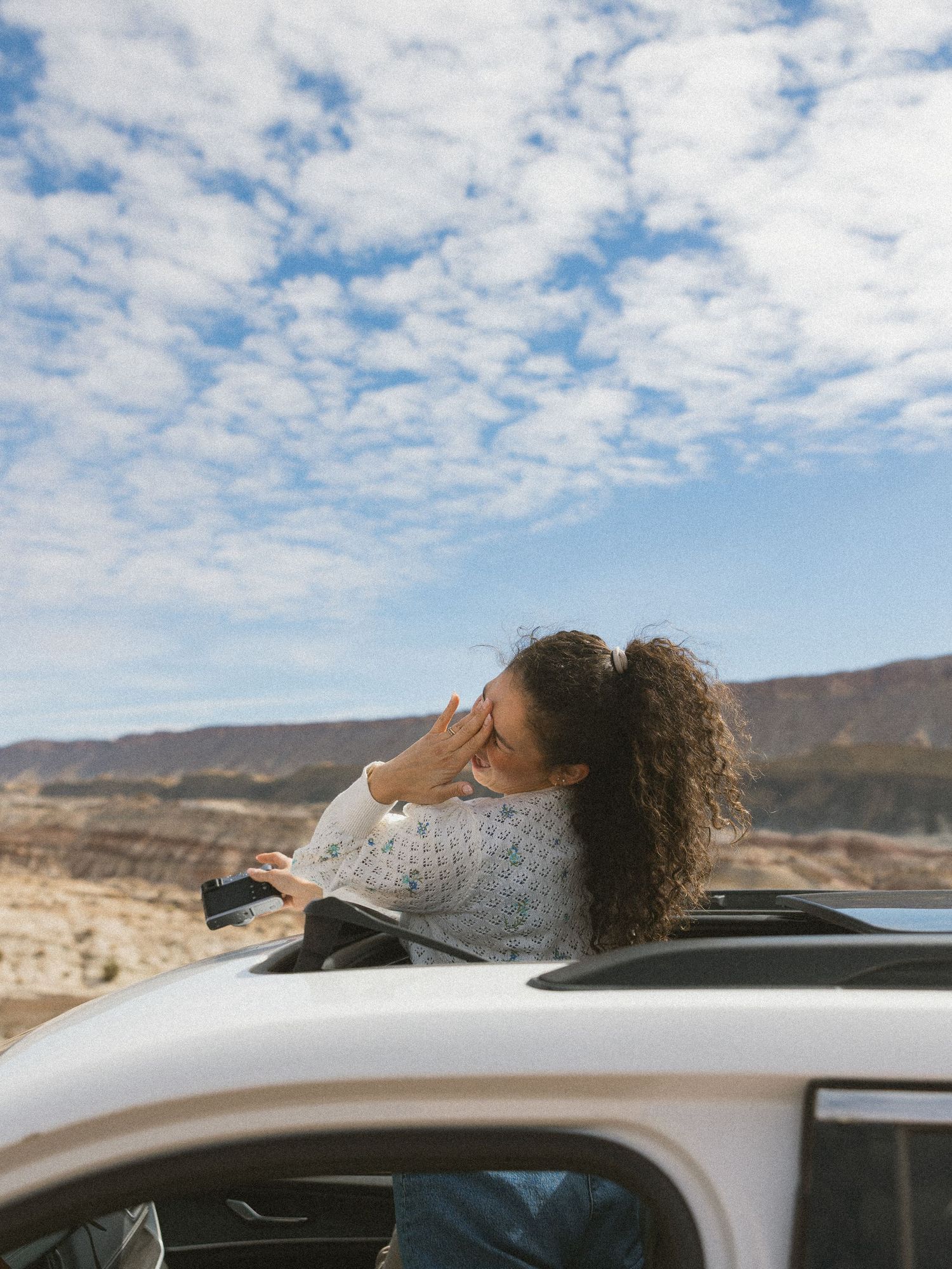 Person enjoying the view through car sunroof in desert landscape under cloudy sky.