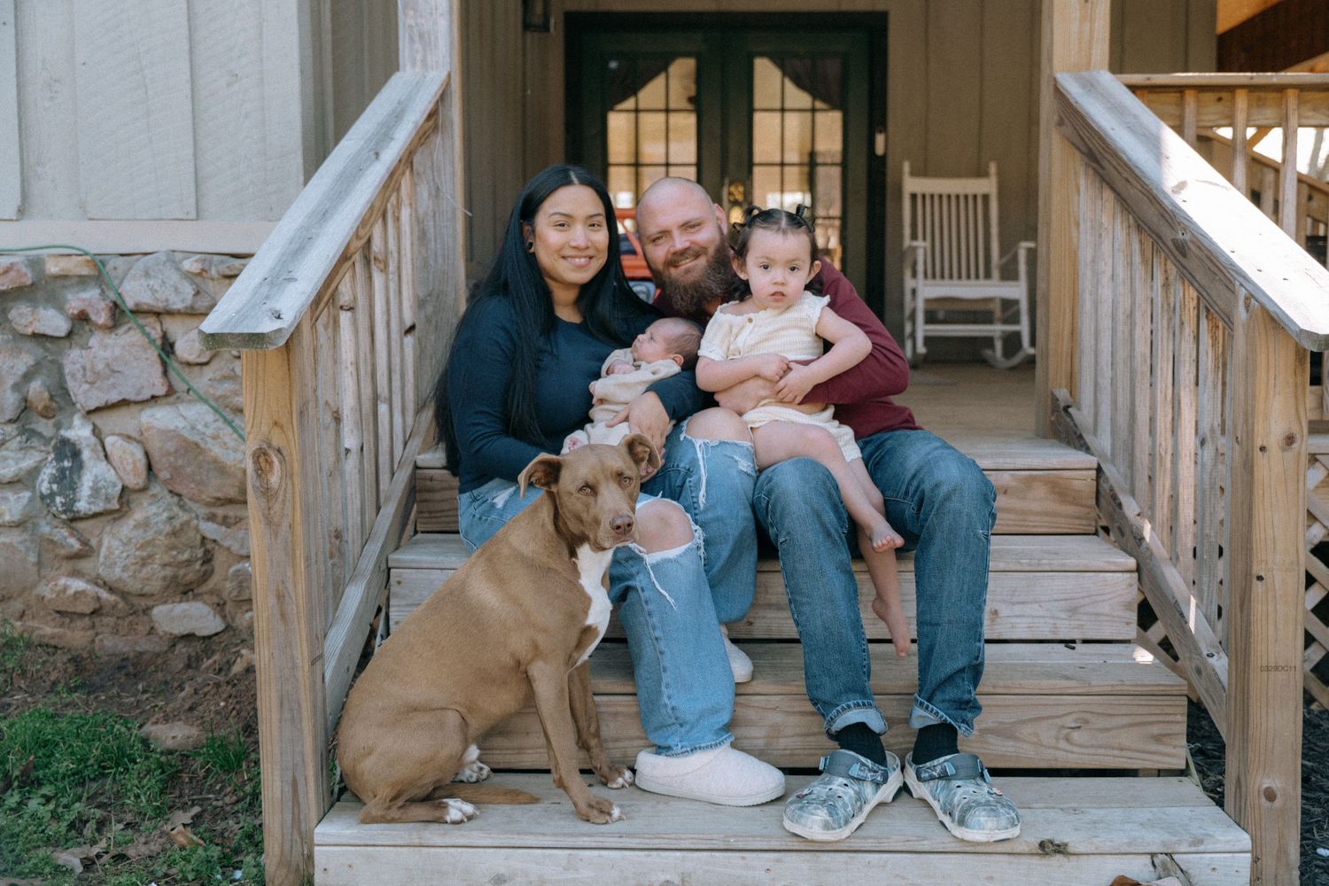 Family sitting together on wooden porch steps with their friendly dog.