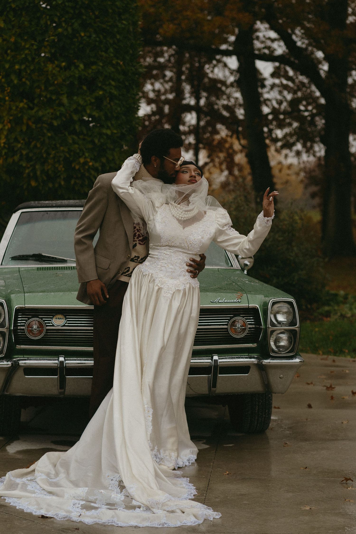 Romantic couple in wedding attire share intimate moments by a vintage car during an autumn photoshoot.