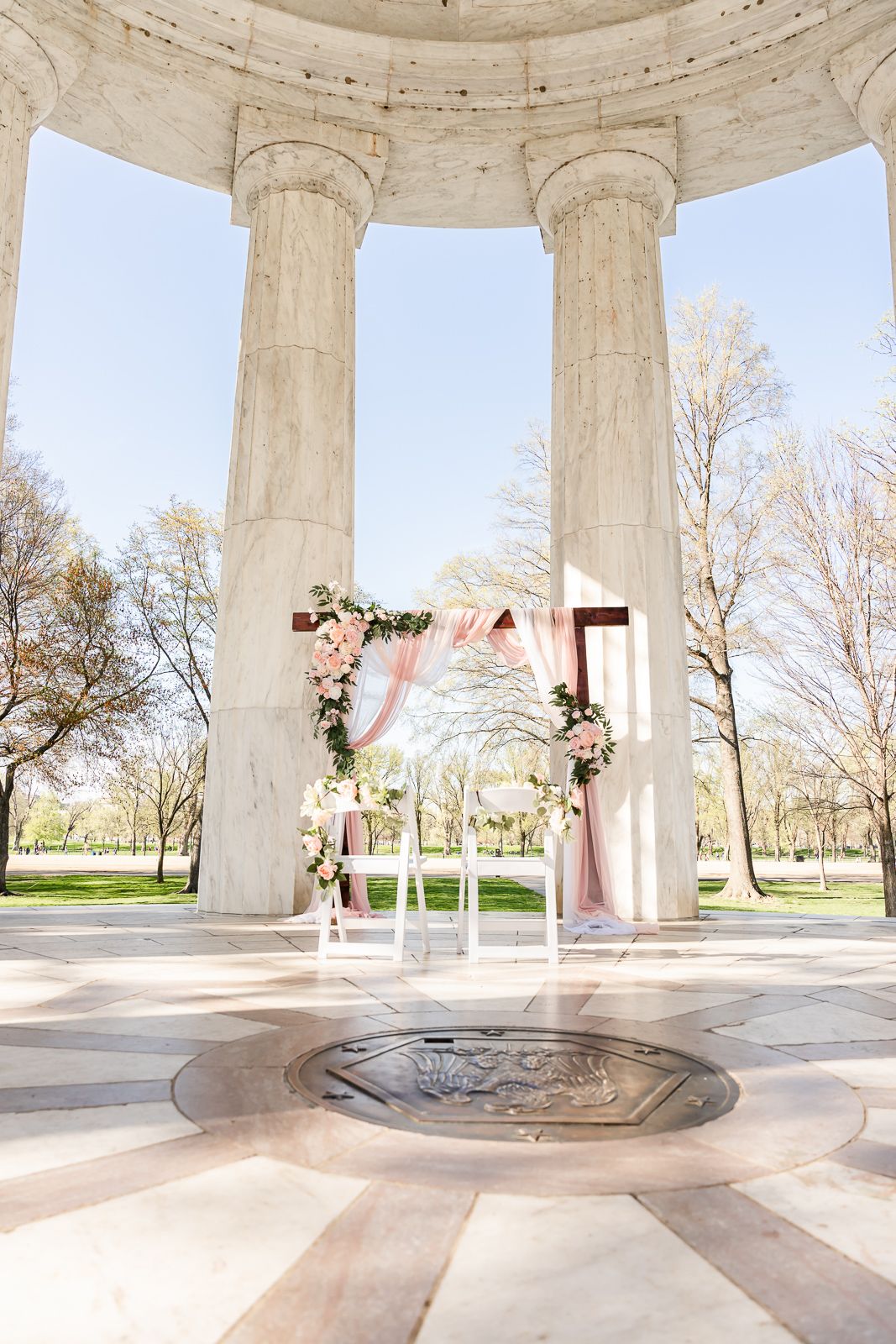 Wedding ceremony arch with pink floral decor inside a classical stone gazebo. wedding photographer videographer