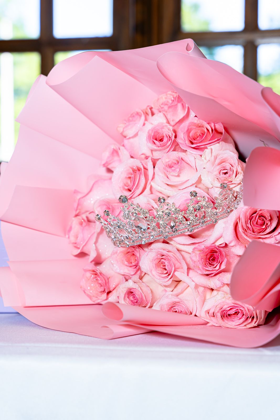 Pink rose bouquet wrapped in paper with a sparkling tiara crown nestled among the flowers.