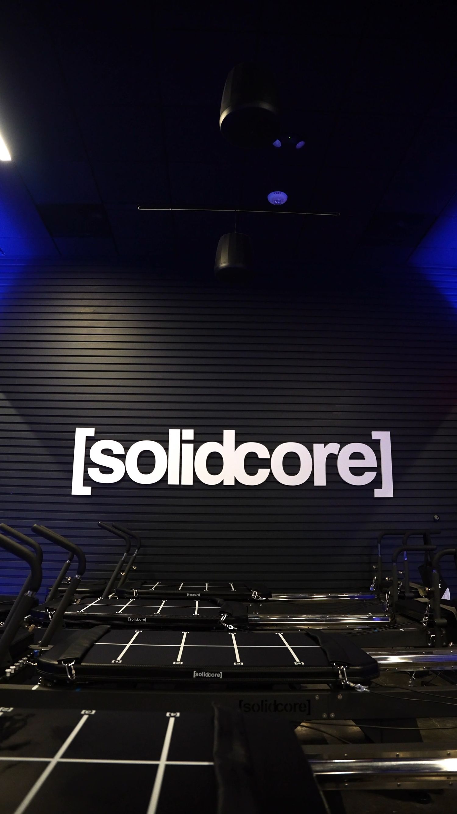 Interior view of a dark fitness studio with trampolines and Solidcore branding illuminated on the wall.